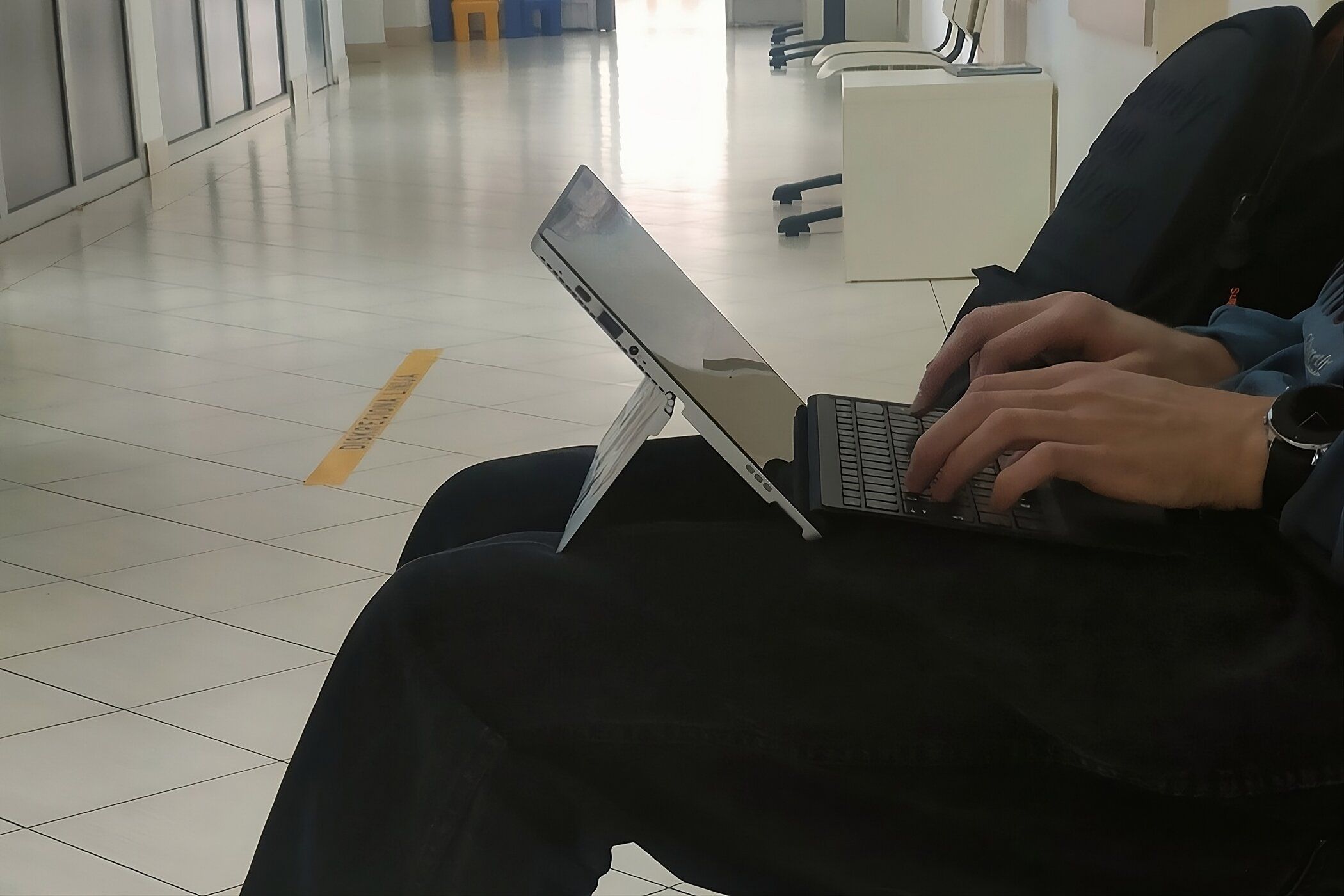 A person typing on a 2-in-1 laptop on their lap.