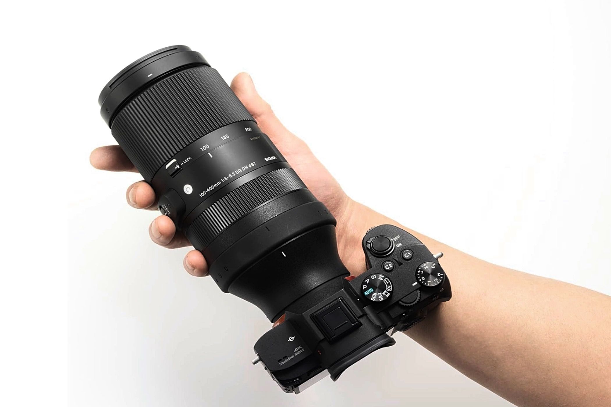 A person&rsquo;s hand holding a Sigma 100-400mm F5-6.3 DG DN OS Contemporary lens mounted onto a camera.