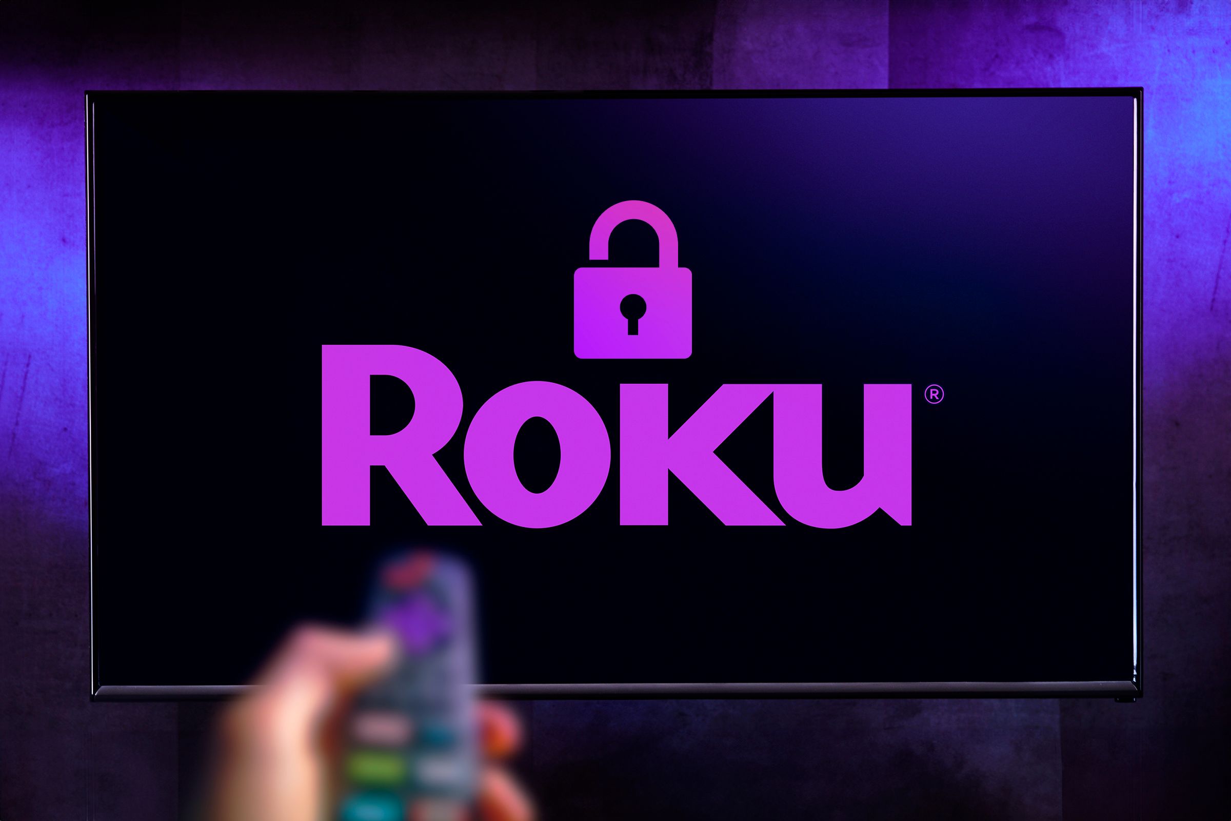 TV with the Roku logo with a padlock and a hand holding a remote control.