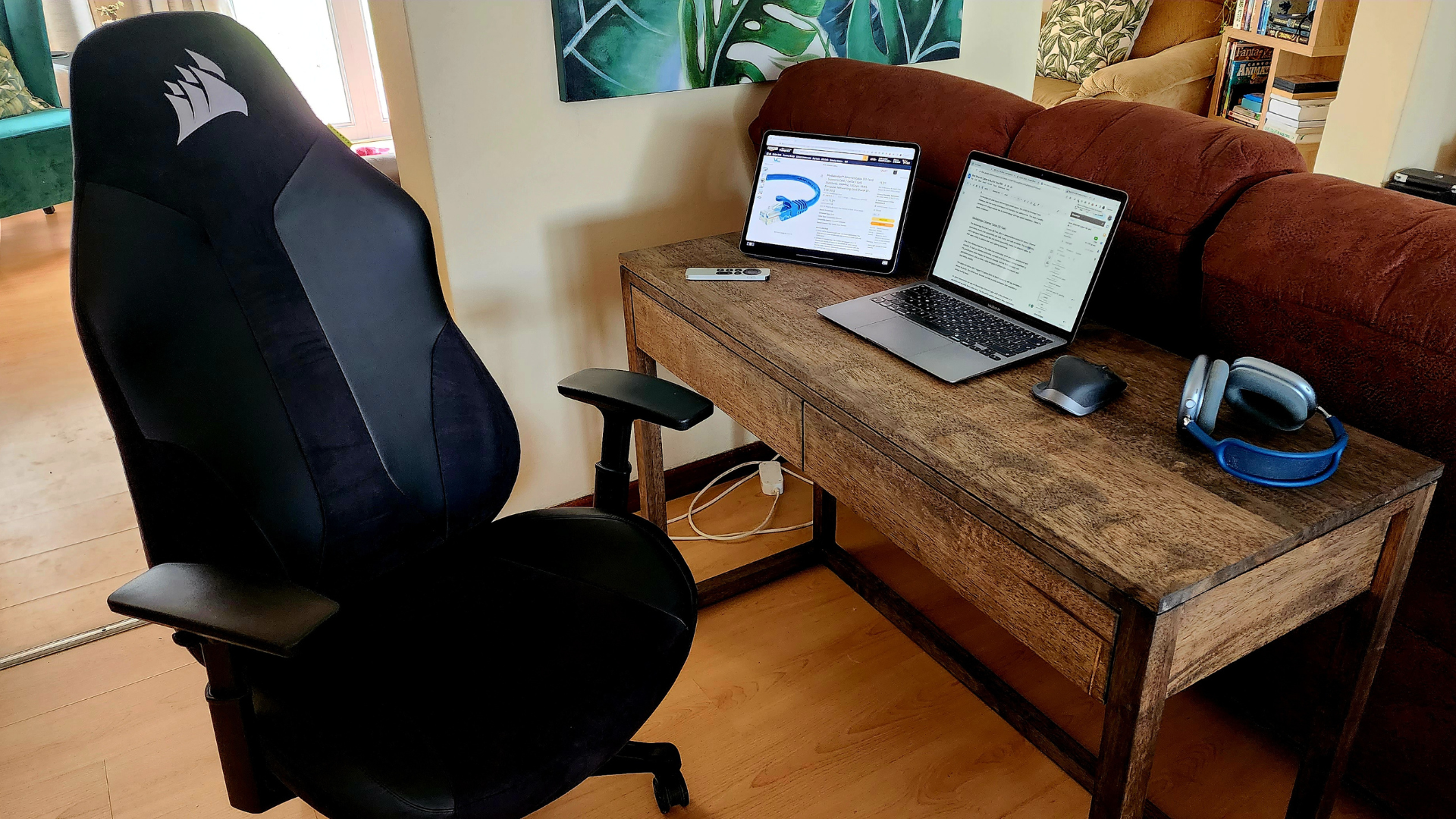 A desk With a MacBook and iPad next to some Airpods Max and an Apple TV Remote