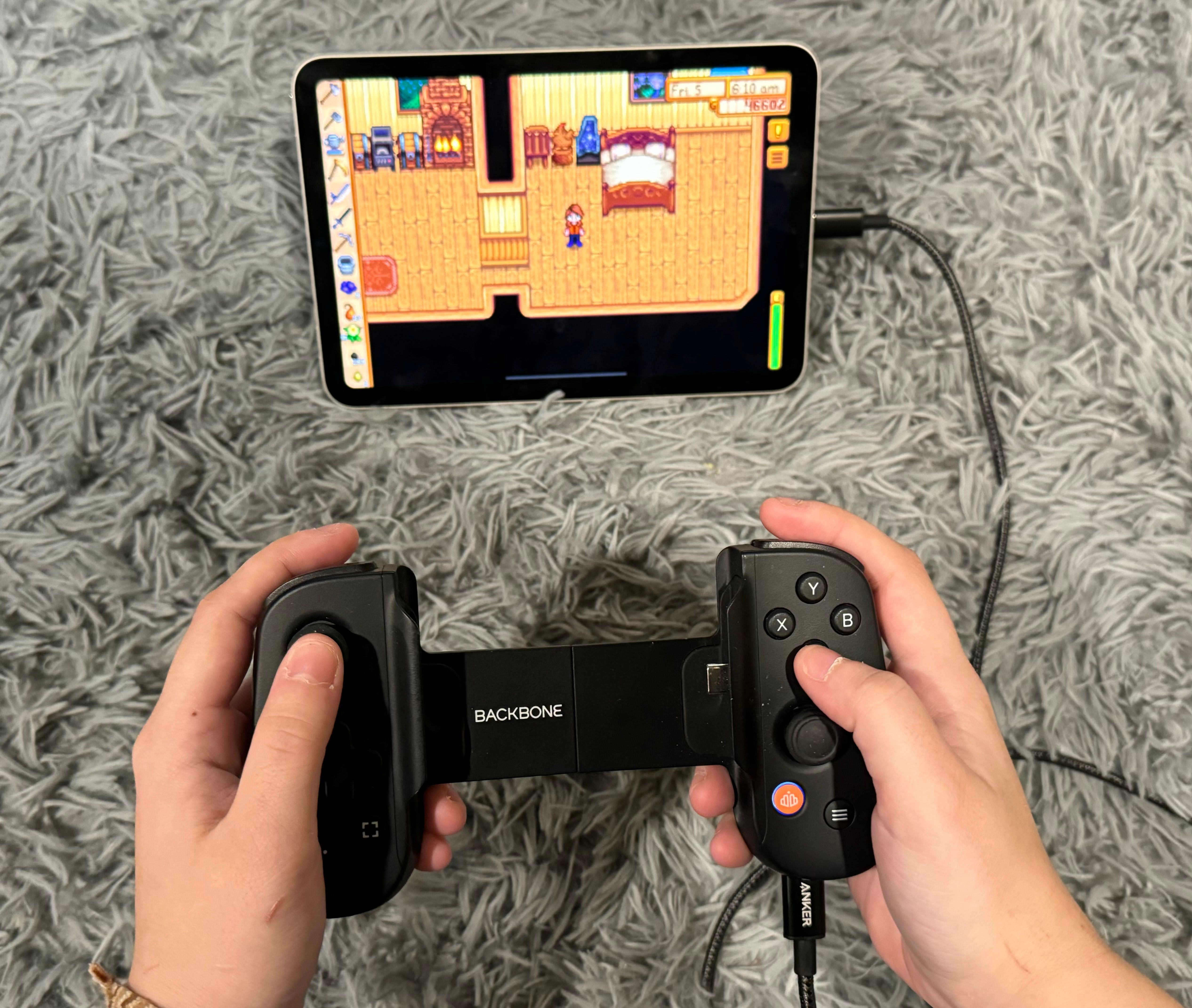 Person holding Backbone game controller connected to iPad mini, with Stardew Valley playing on screen.