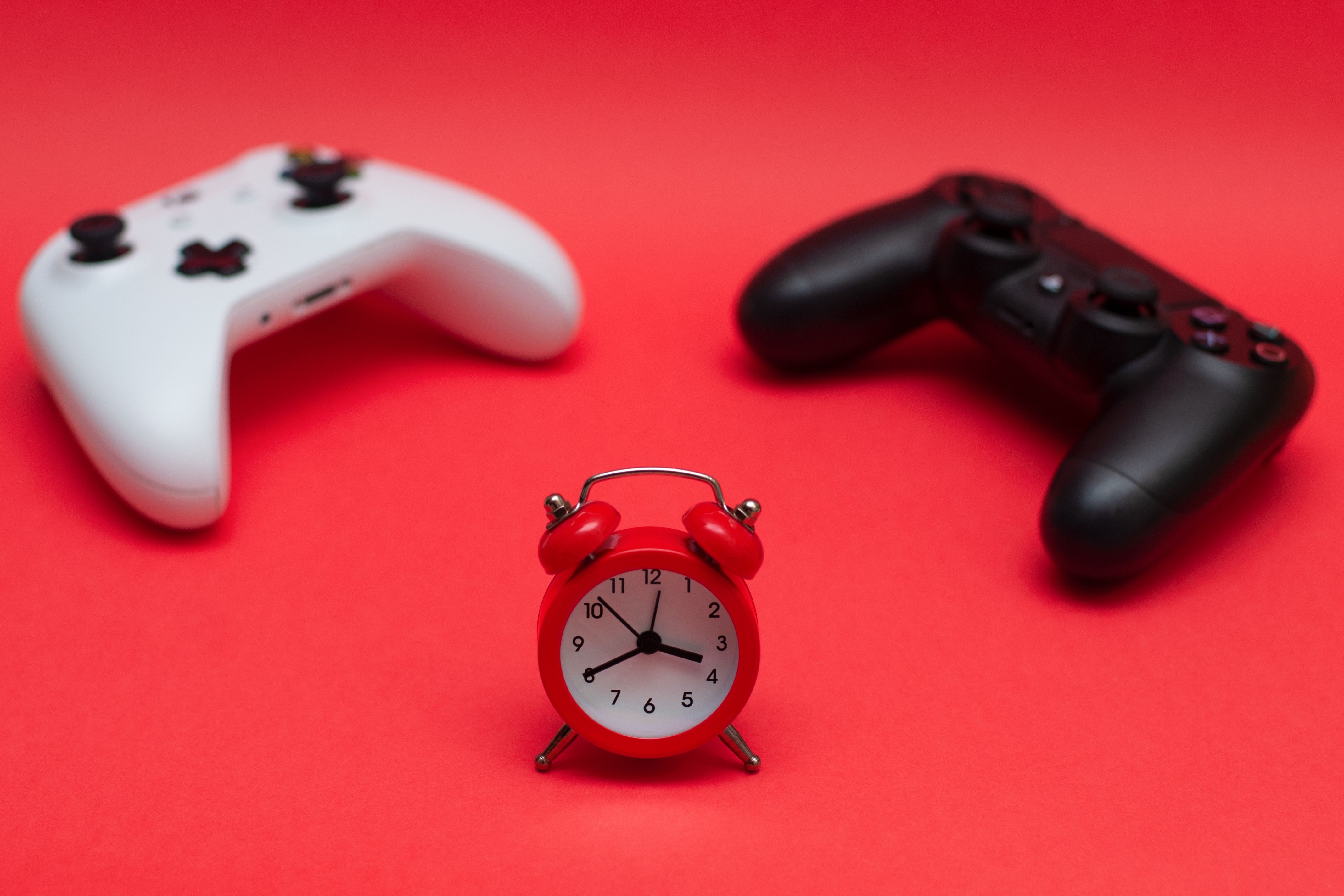 Two game console controllers with an alarm clock between them on a red background.