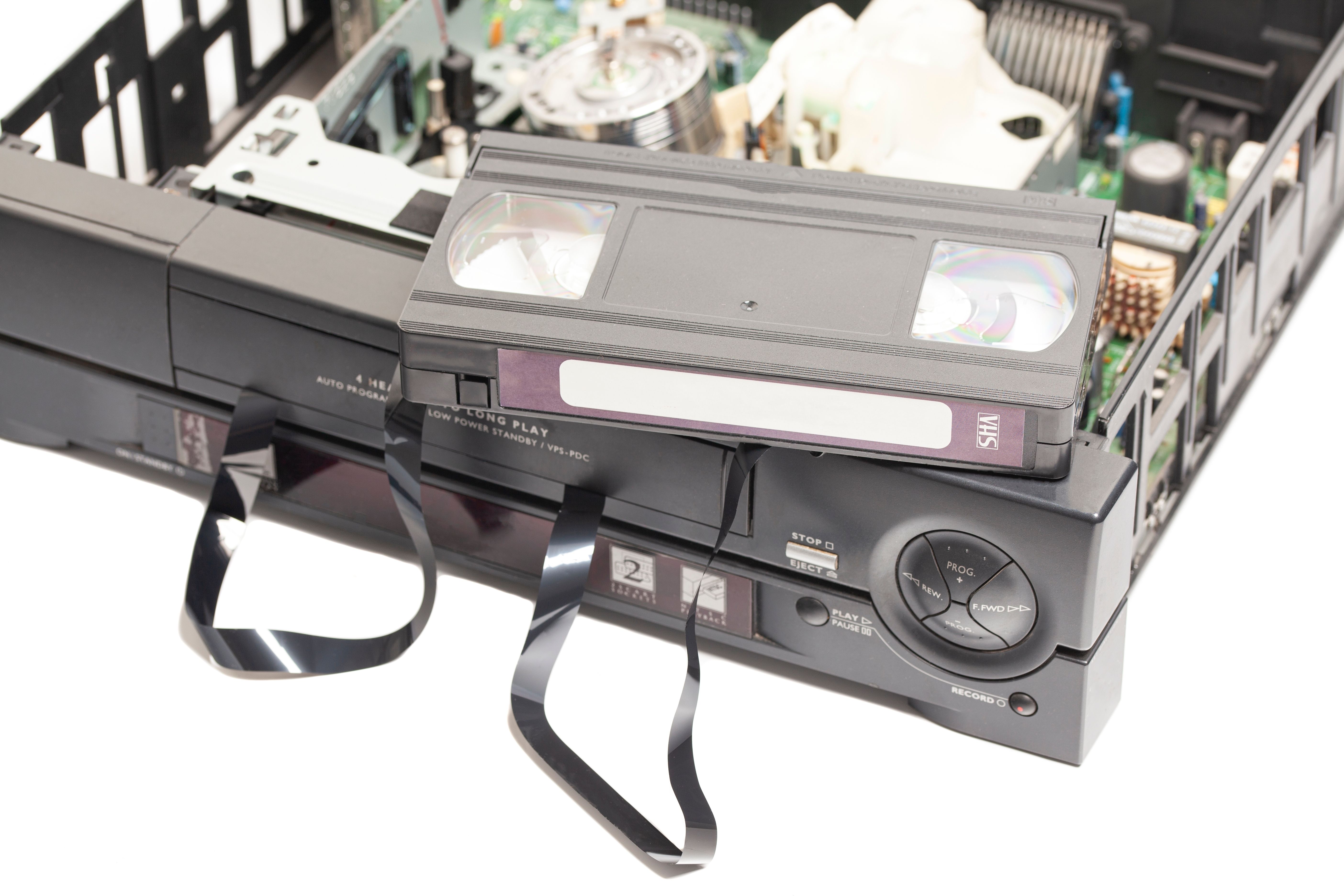 Retro disassembled video cassette recorders with broken VHS cassette with unwound tape isolated on white background.