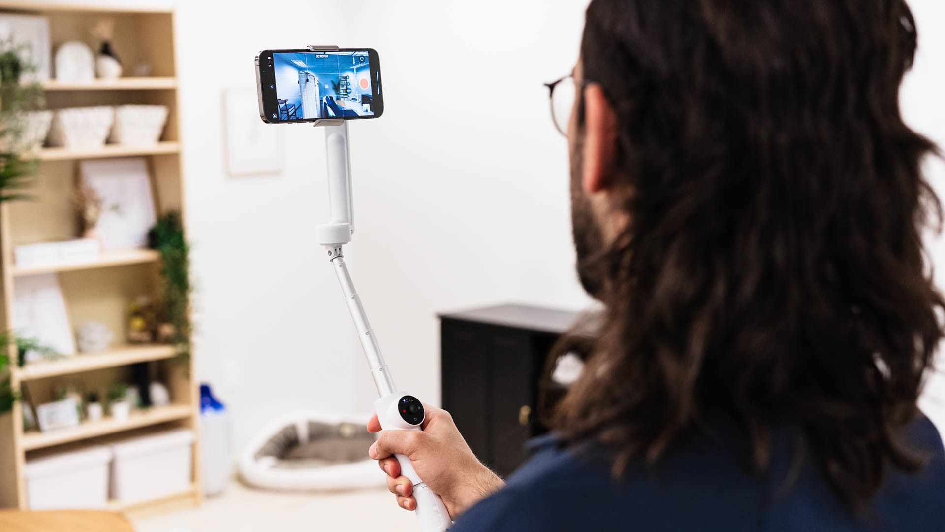 A man with a selfie-stick shooting a video in his home.