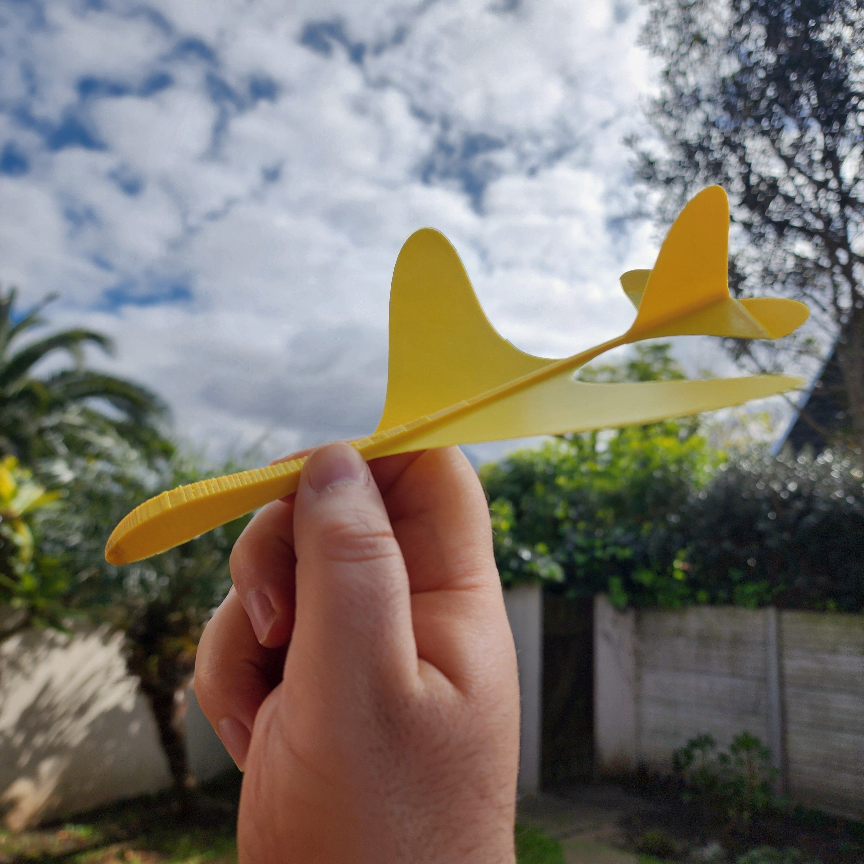 A yellow 3D printed glider held in a person&rsquo;s hand.