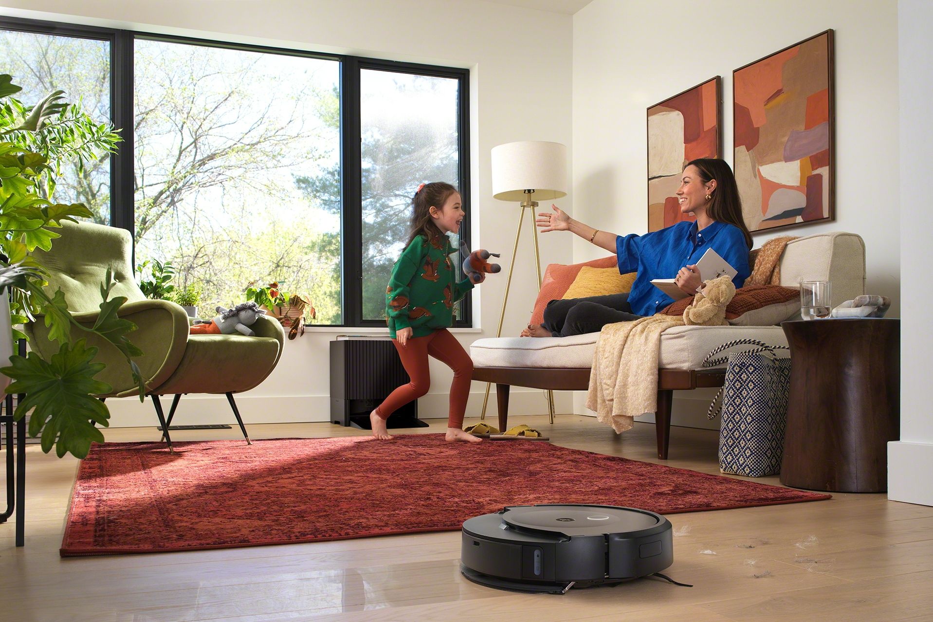 Mother and daughter in a living room, with iRobot's Roomba robot cleaning the floor.