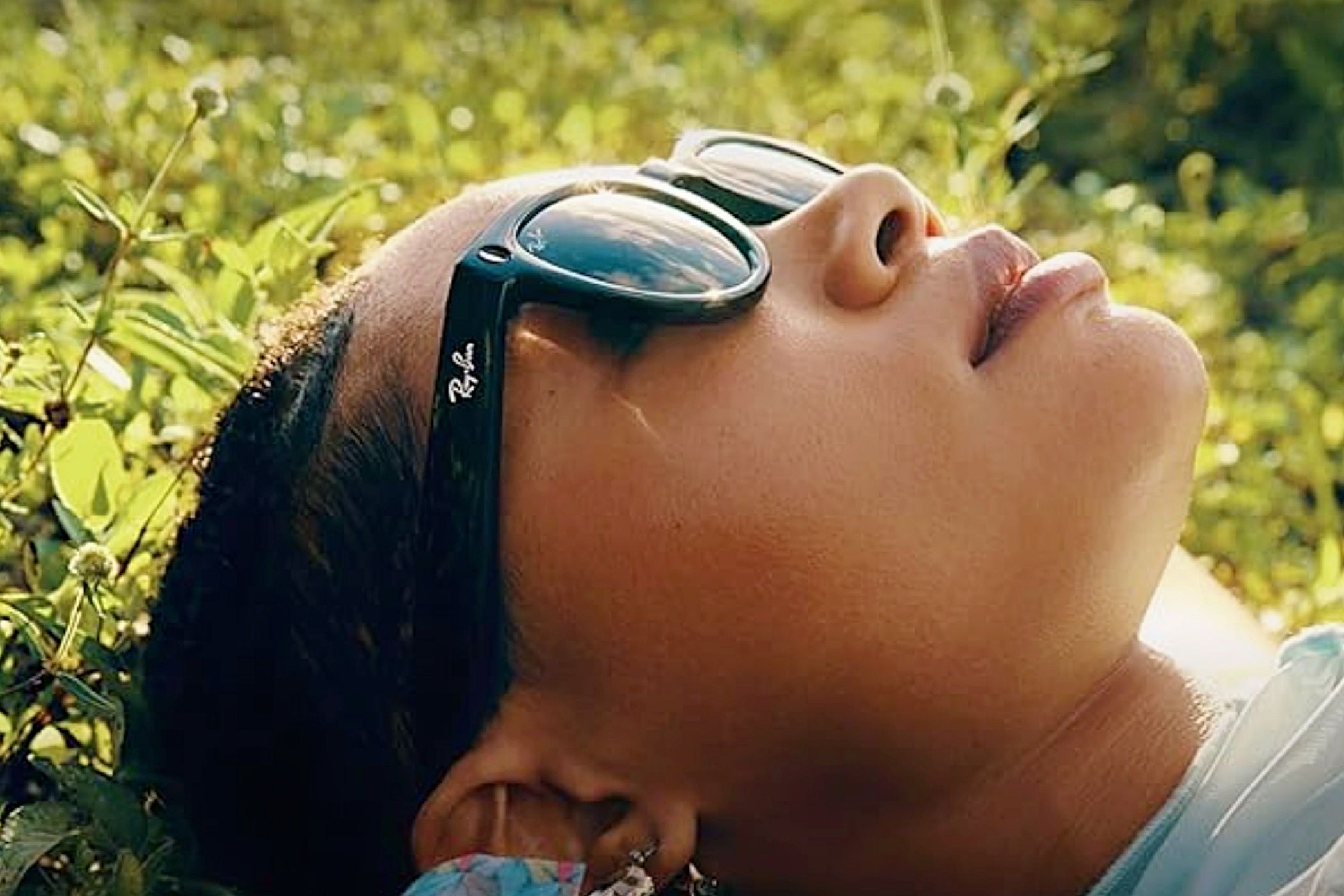 A woman lying on the grass looking at the sky wearing a pair of Ray-Ban Meta Smart Glasses