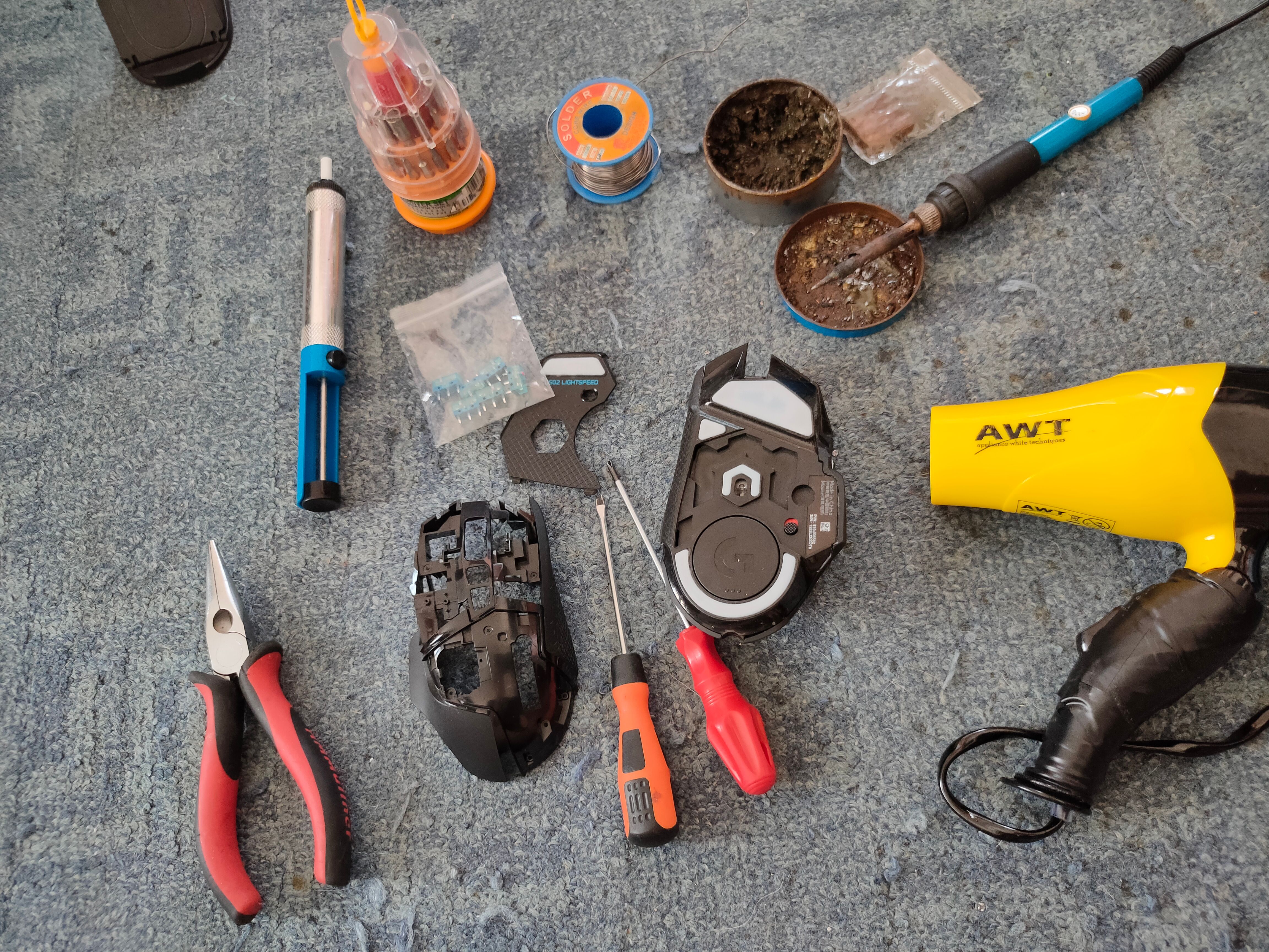 A Logitech G502 mouse surrounded with replacement parts and tools, including a soldering iron.