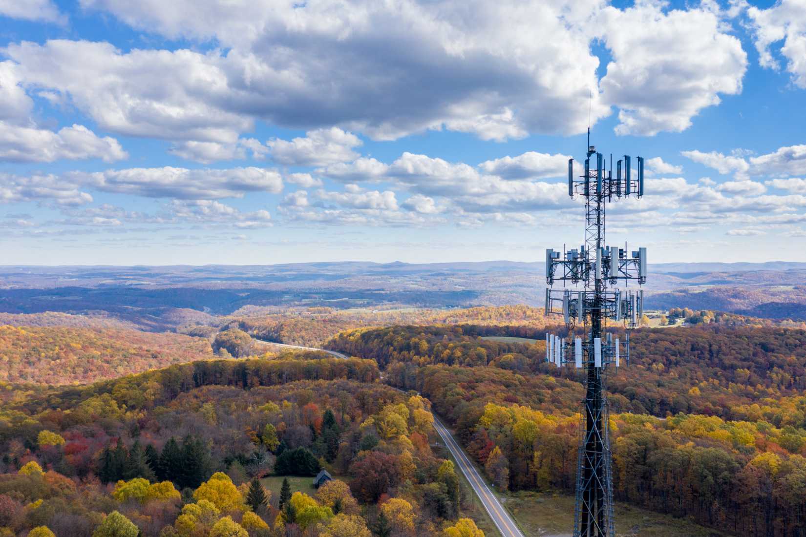 A cell tower over rural West Virginia. Fall trees are running into the distance where they meet a mountain range.