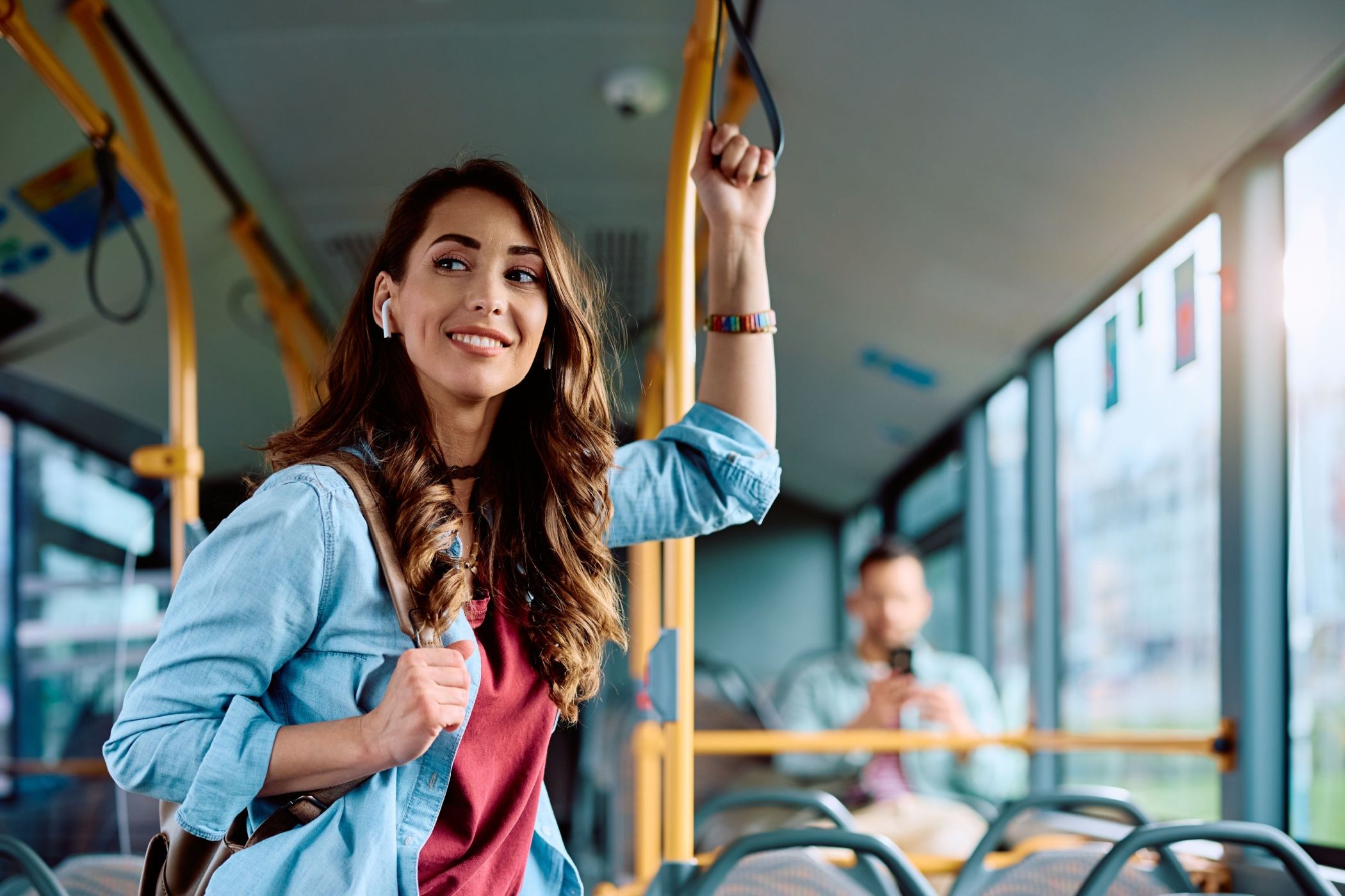 Young smiling woman holding onto a handle while traveling by public bus.