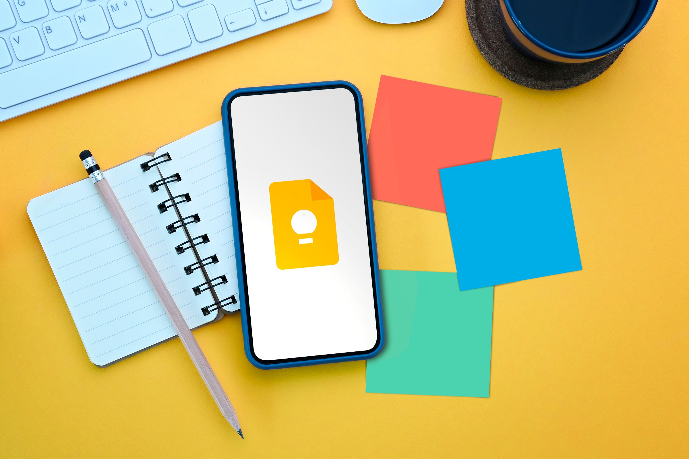 A phone above a notebook with the Google Keep logo and some sticky notes next to it.