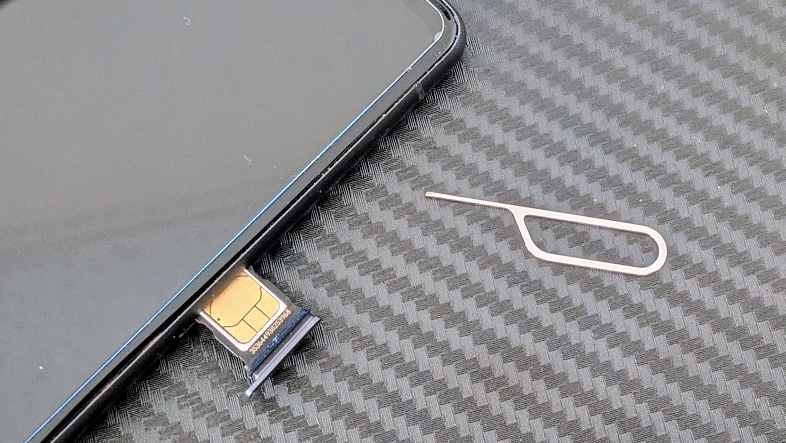 A SIM tool next to a smartphone with the SIM card visible in its tray.