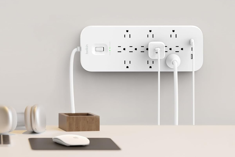 Belkin SRA007 12-outlet surge protector centered on a wall and powering Apple devices.