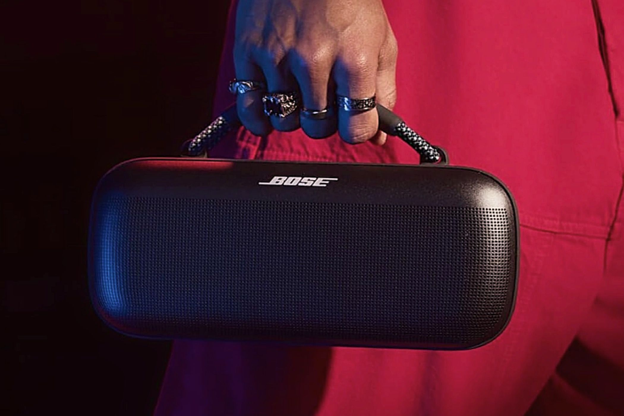 A man in red carrying a Bose SoundLink Max by its handle.