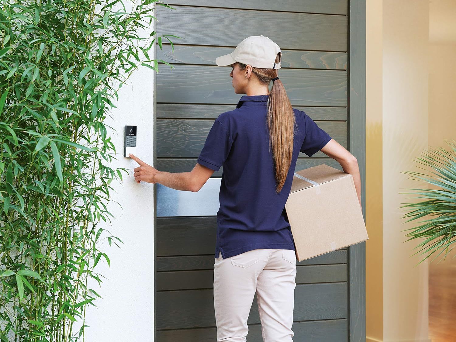 Delivery person ringing the doorbell with a package in her hand.