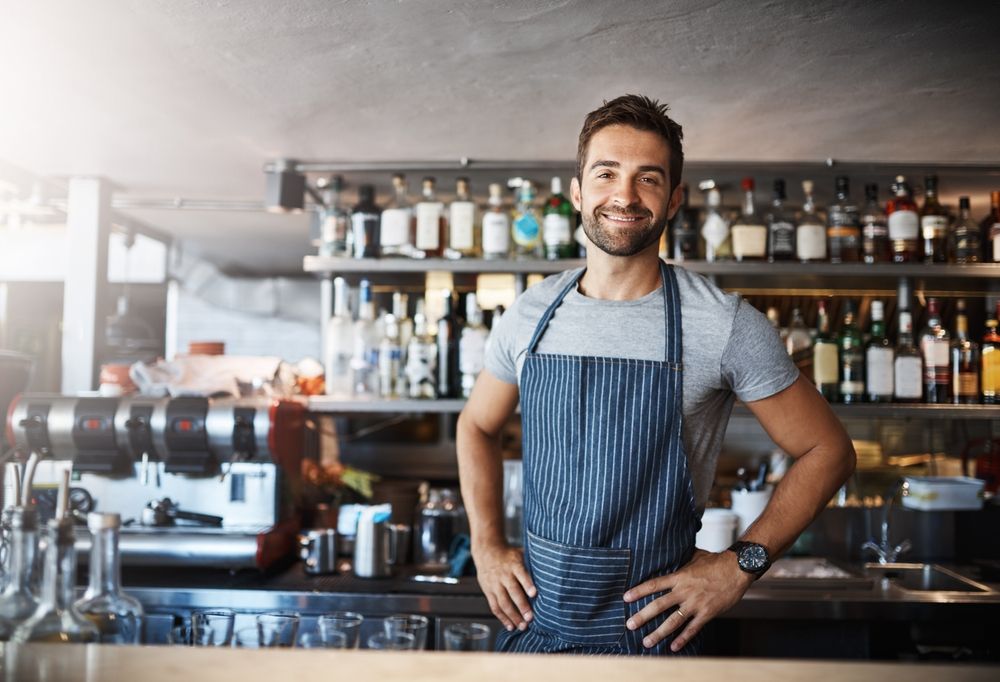 Bartender, man and happy in portrait at counter with service for drinks, cocktails and liquor in restaurant.