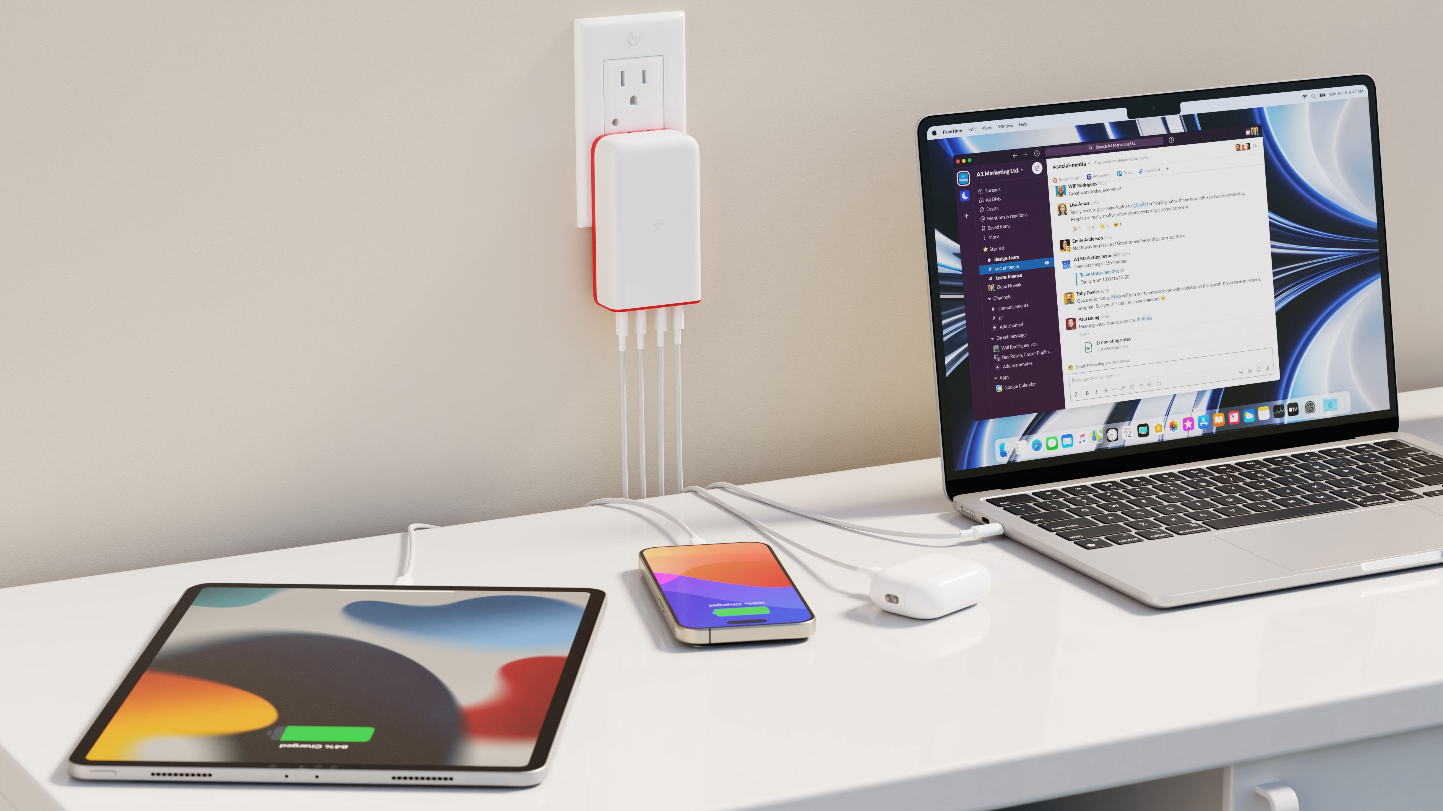 A white desk with an iPhone, iPad, and a MacBook connected to a multi-port charger plugged into a wall socket.