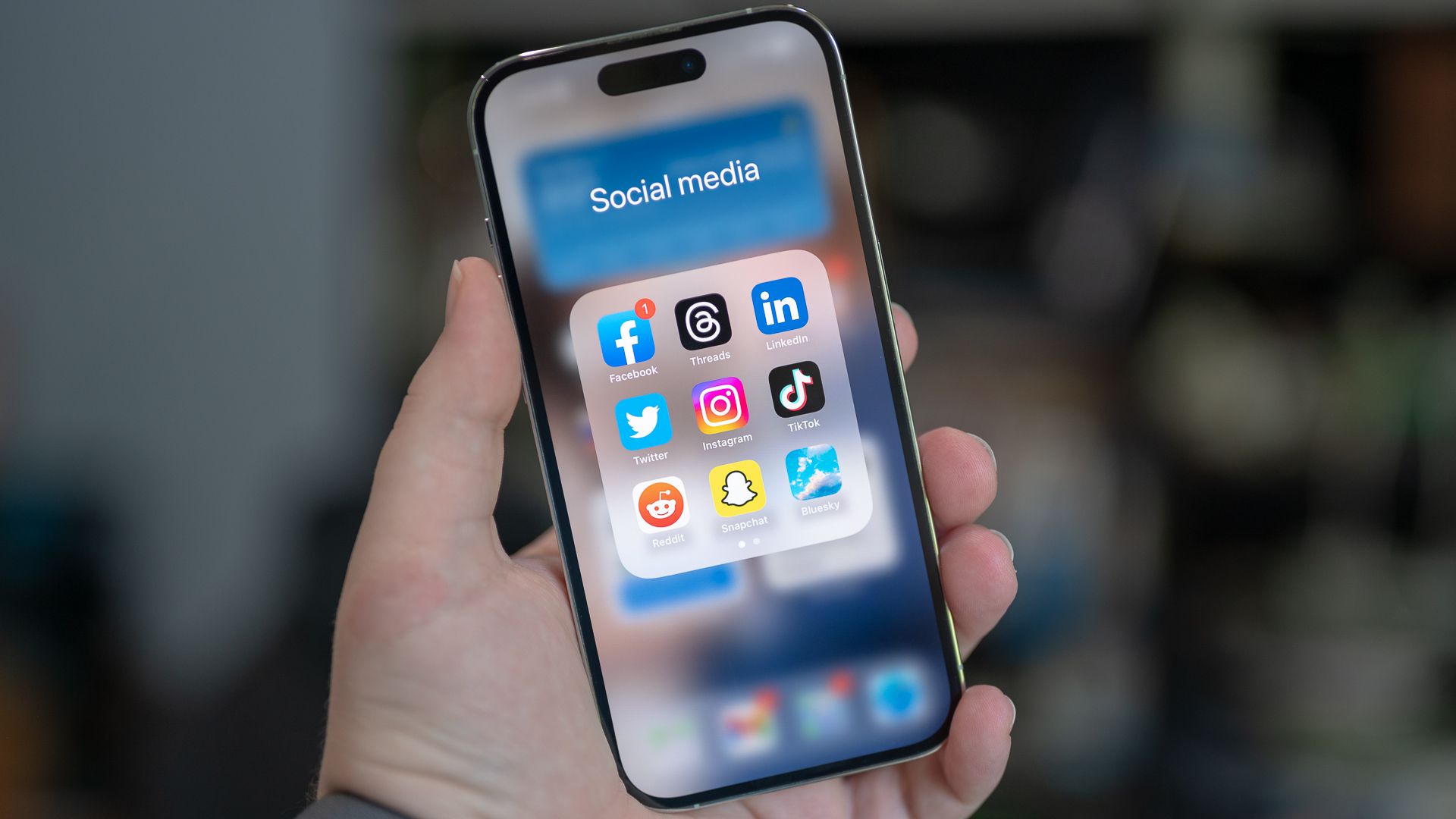 Social media folder on an Apple iPhone 14 Pro with Facebook, Threads, LinkedIn, Twitter, Instagram, TikTok, Reddit, Snapchat, and Bluesky apps.