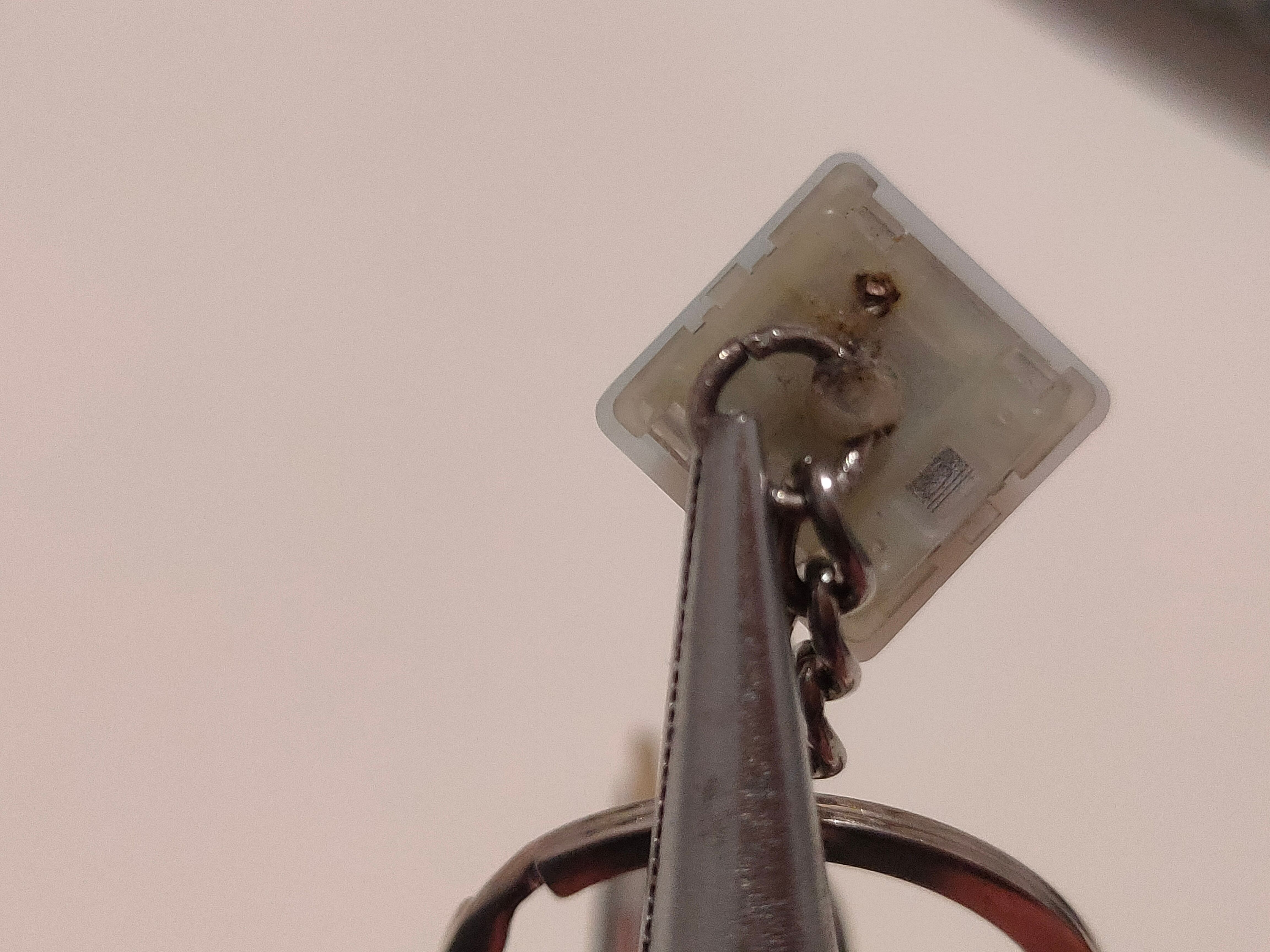 Pliers holding a closed jump ring to a keyboard switch to create a keychain charm.