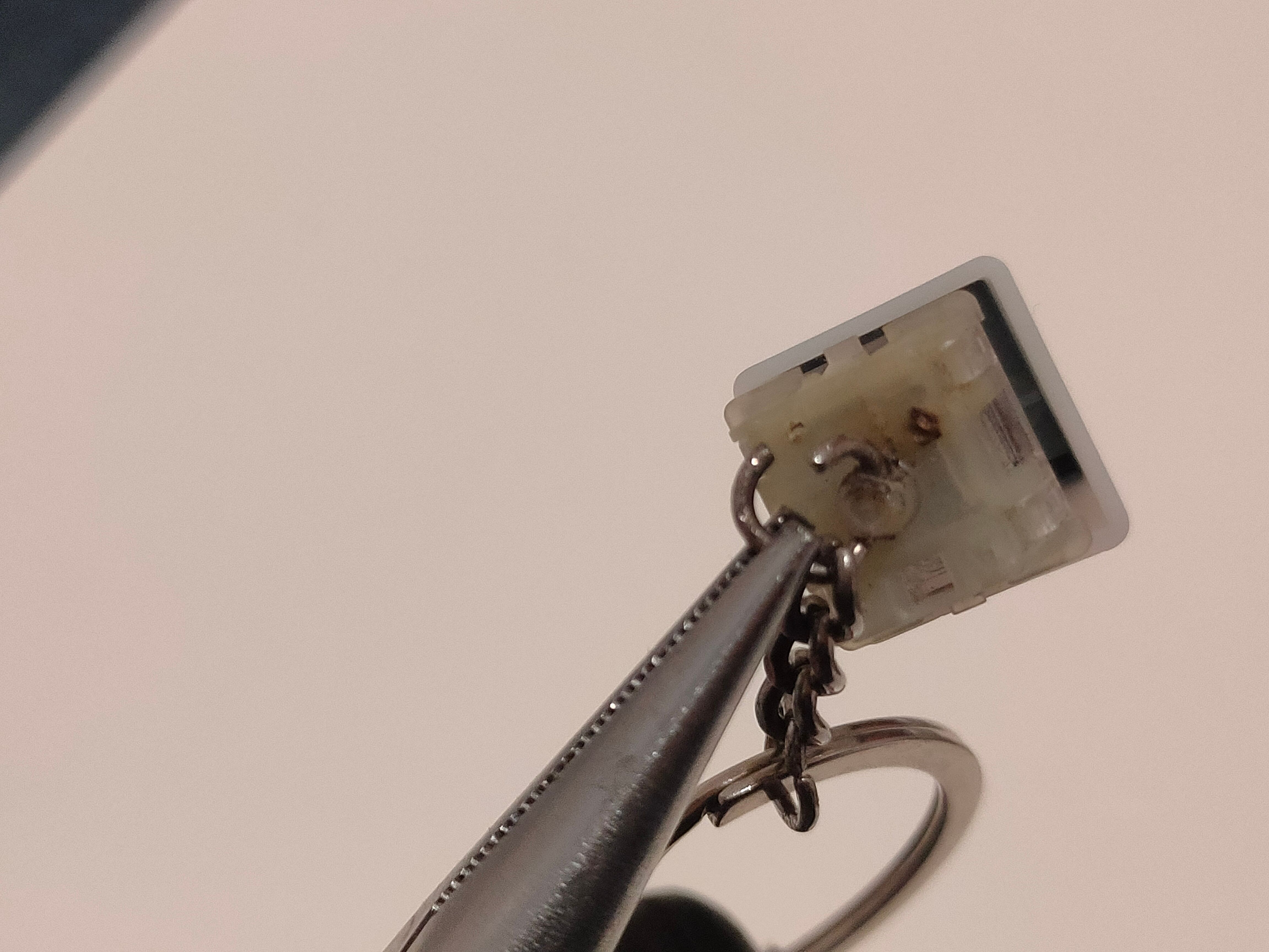 Pliers holding an open jump ring to a keyboard switch to create a keychain charm.