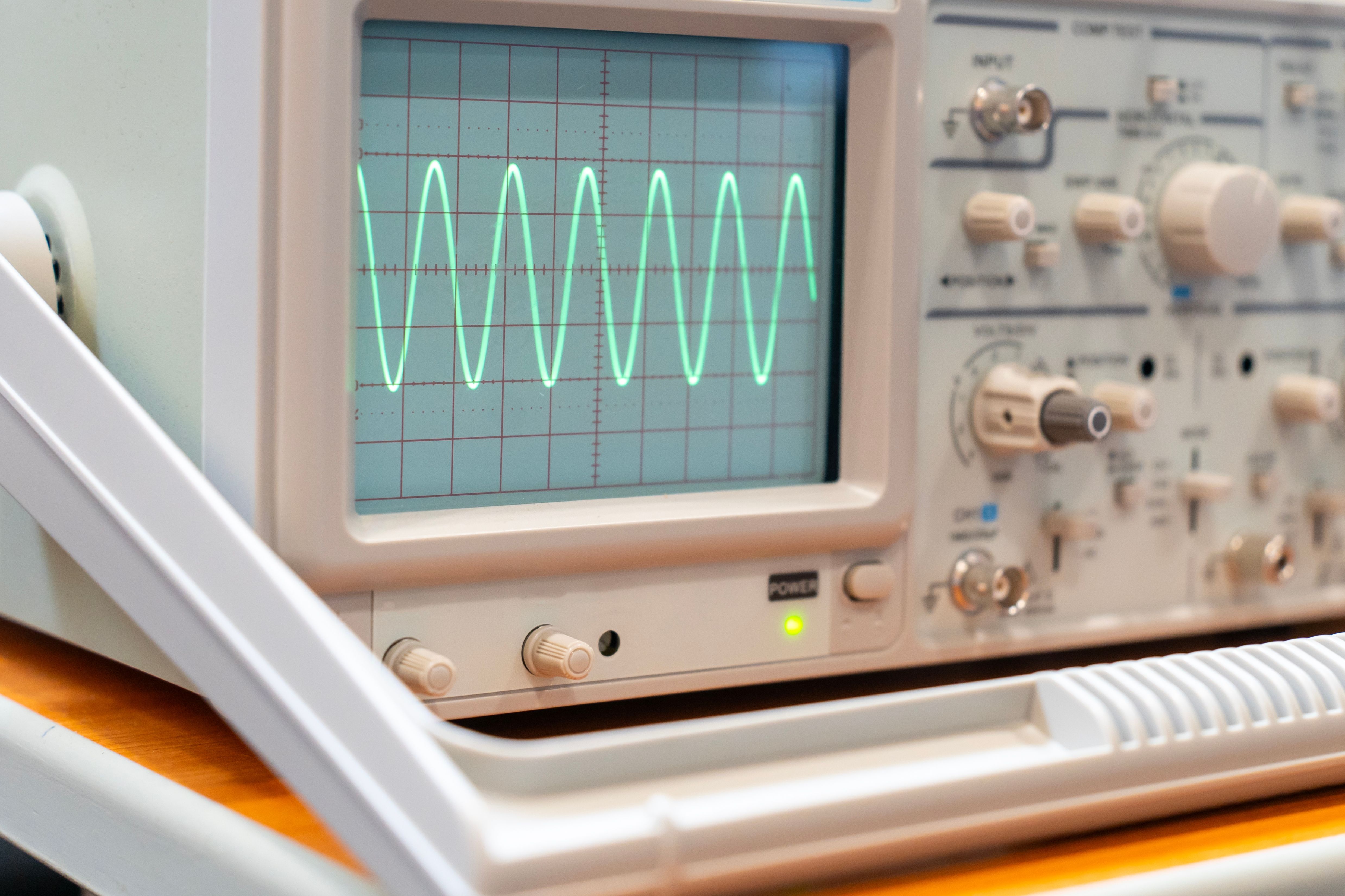 Green sine waves on the screen of a multi-button oscilloscope.