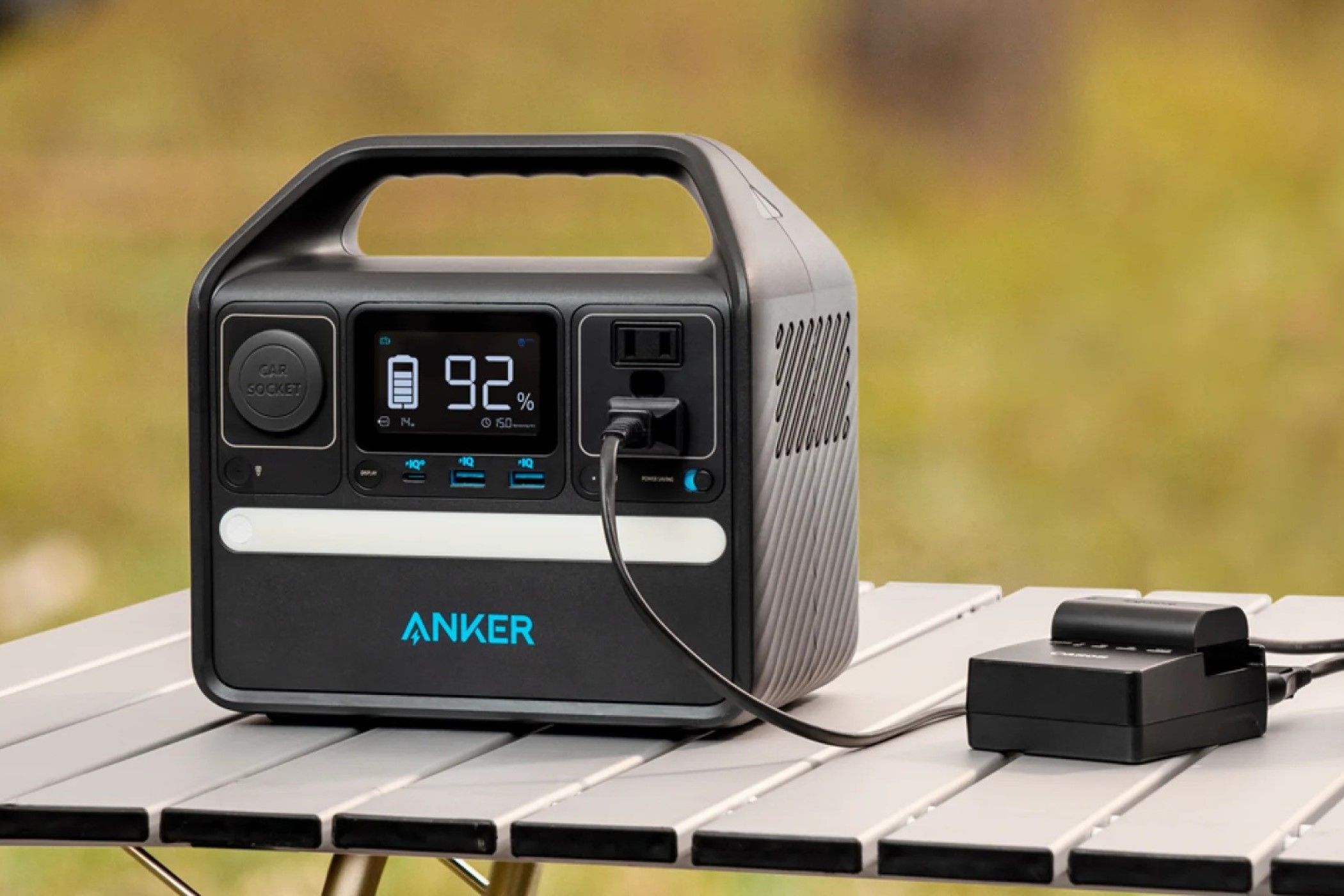 Anker 521 Portable Power Station sitting on a table with a battery charger hooked to it. 