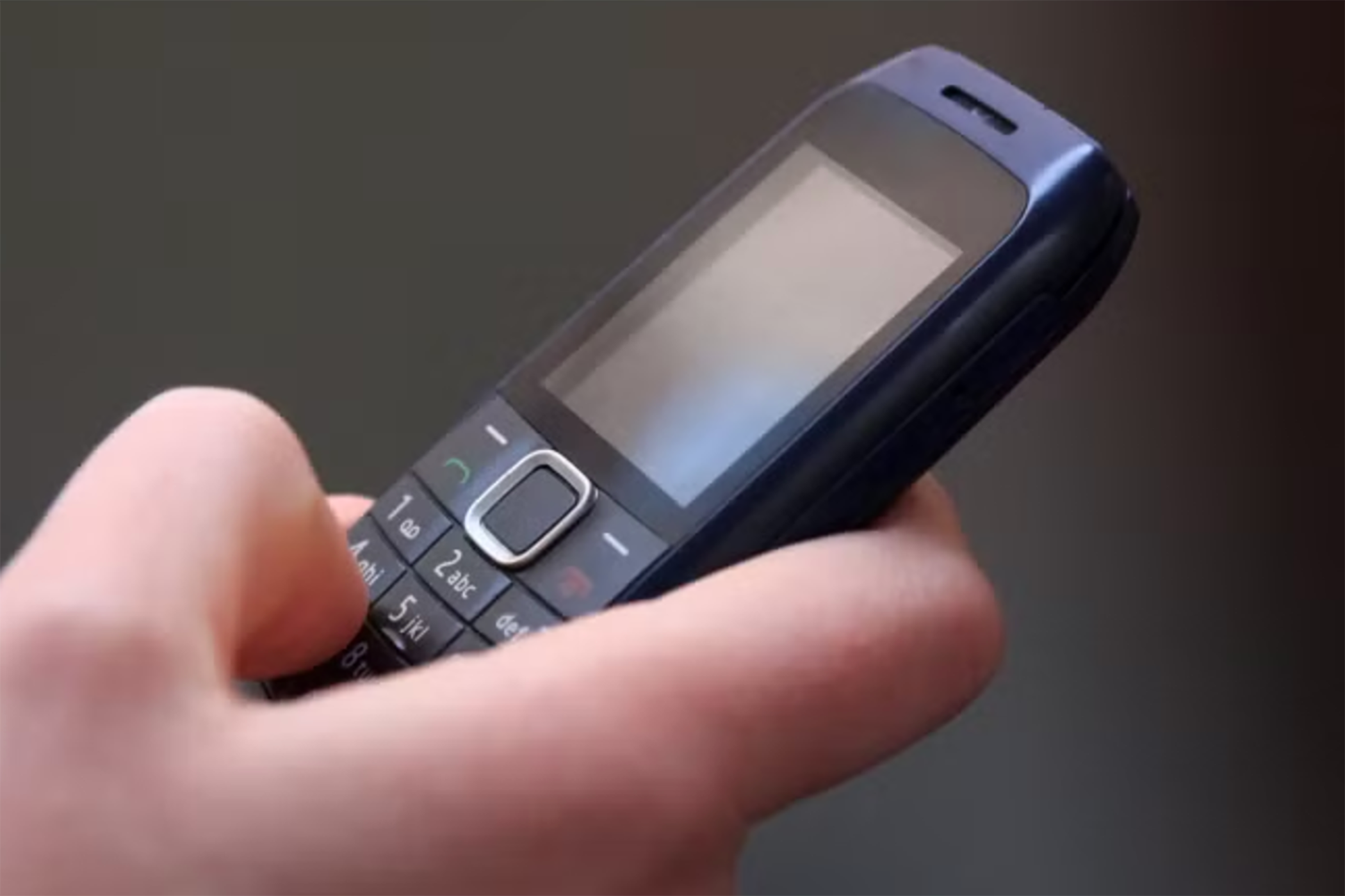 A Nokia cell phone from the 1990s in a person's hand with a black background. 