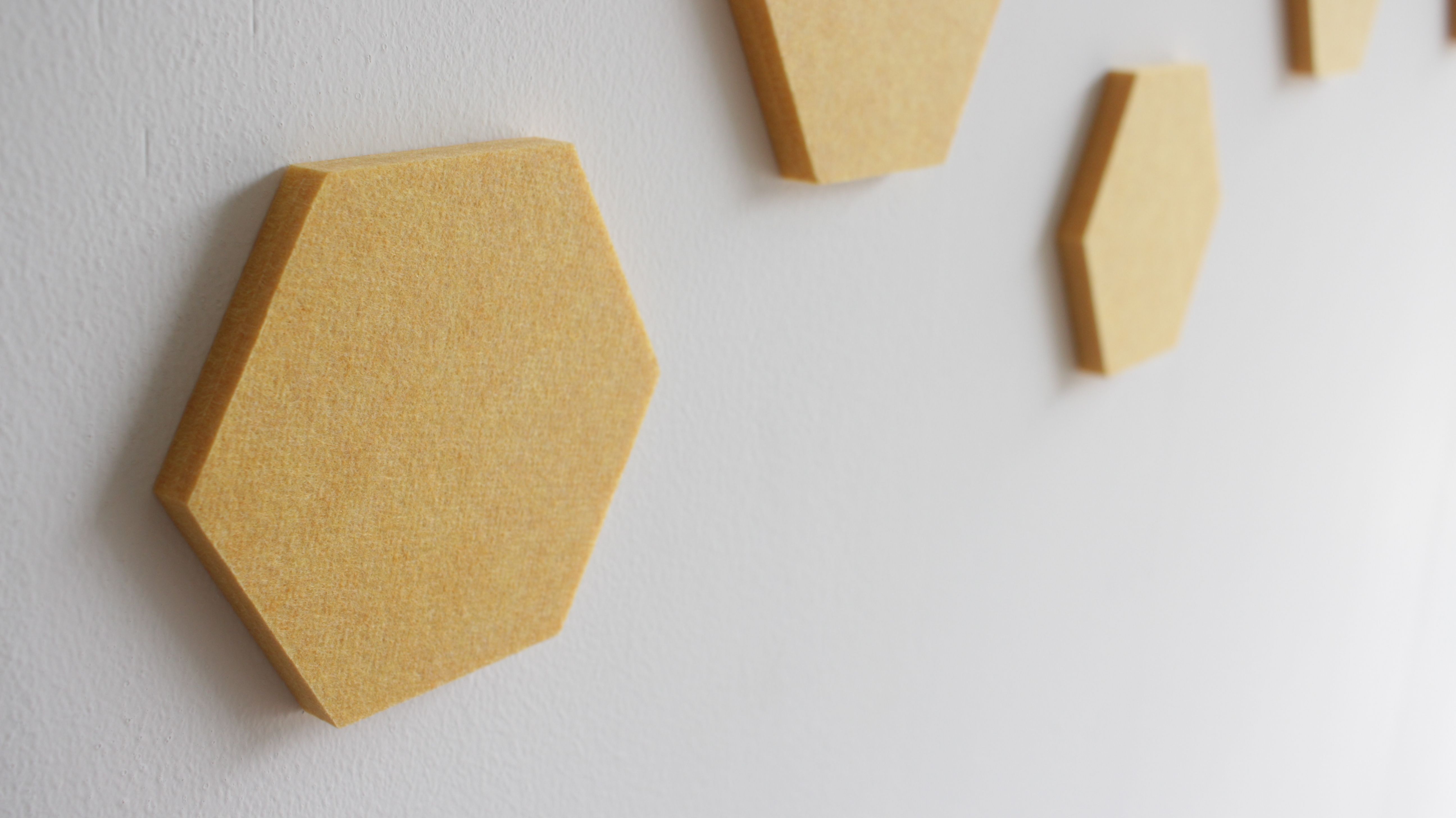 Close-up of a yellow hexagonal acoustic panel attached to the wall.