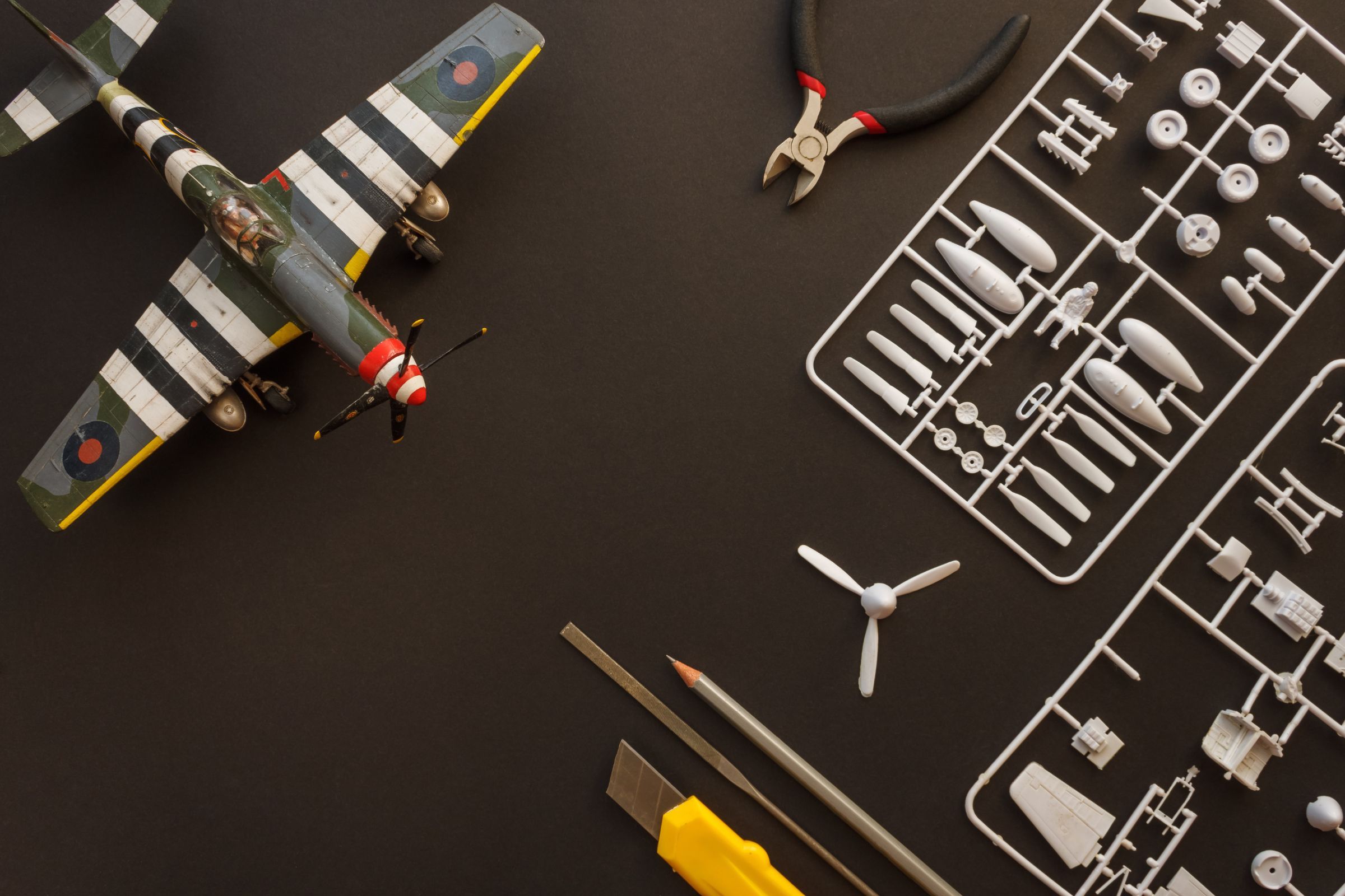 A completely painted plastic model airplane next to model kit parts in a cast frame, with various modeling tools.