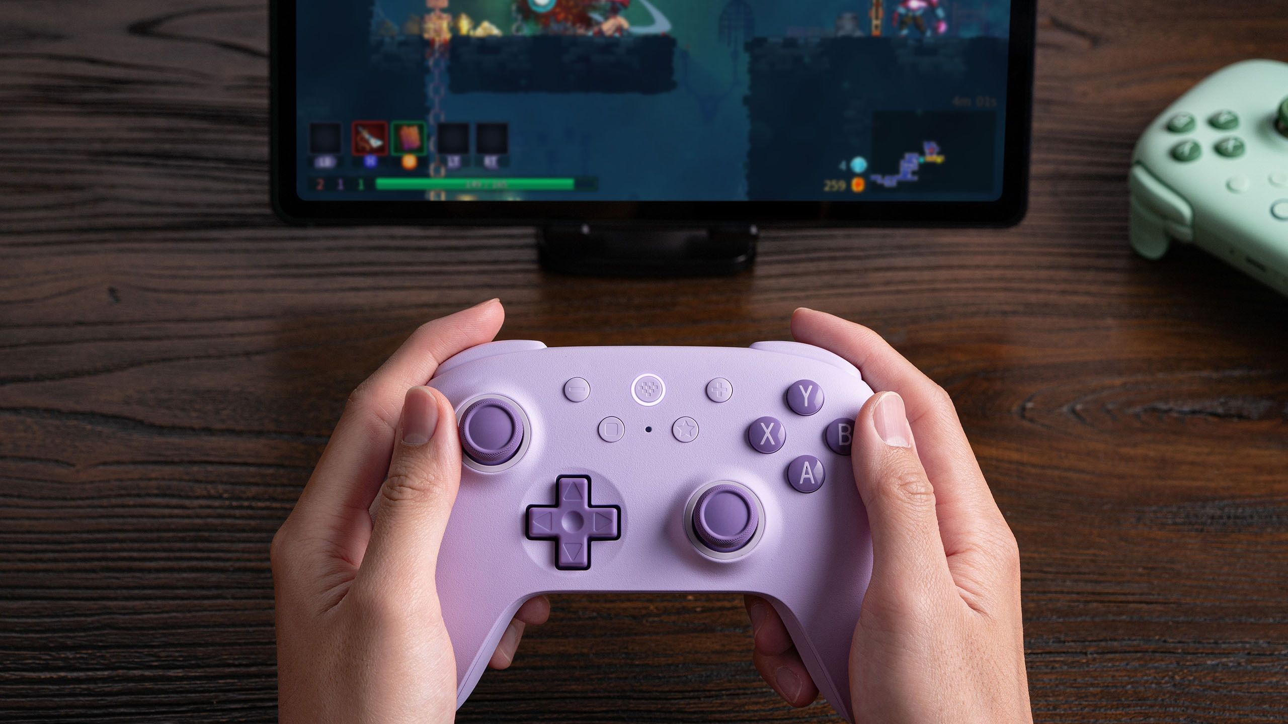 A person holding an 8BitDo Ultimate 2C Wireless Controller and playing Dead Cells on a tablet. 