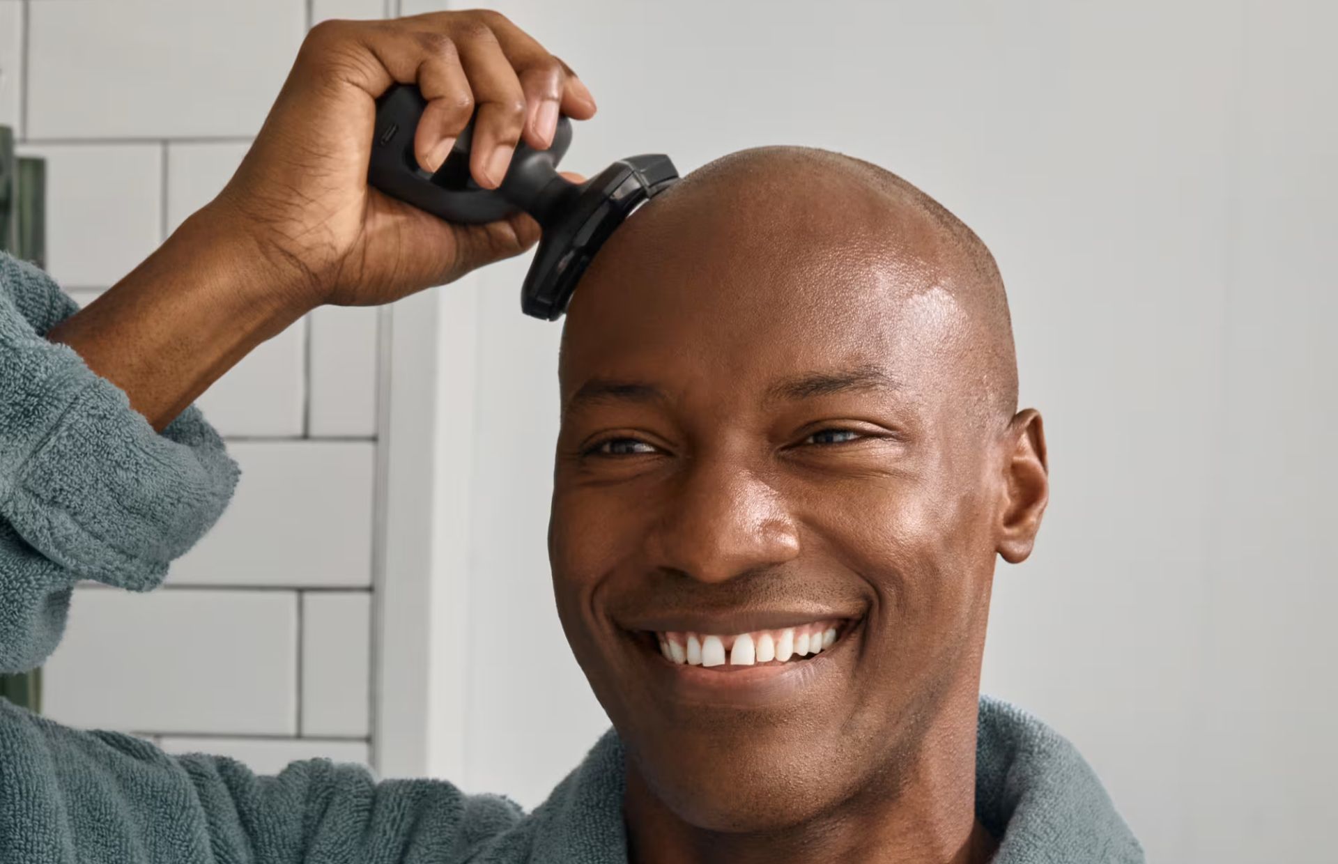 Smiling man using a dome shaver head razor in a bathroom. 