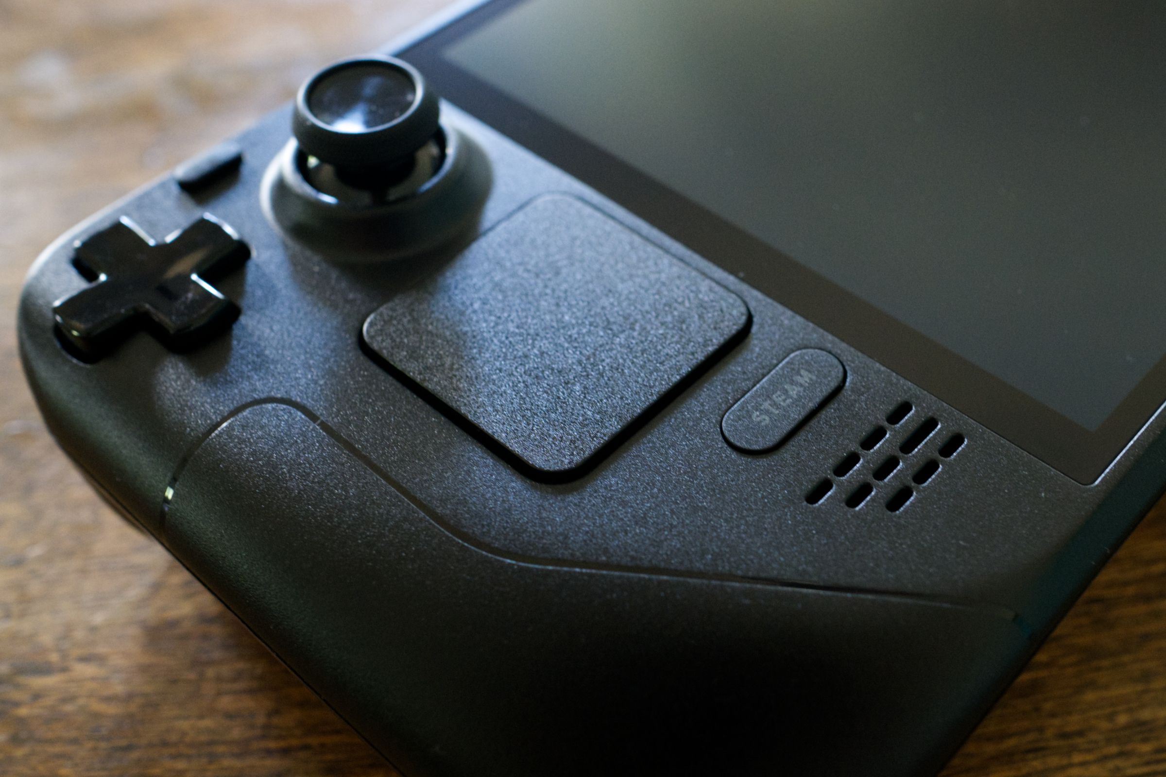 Steam Deck OLED on a wooden table with the Steam button in focus.