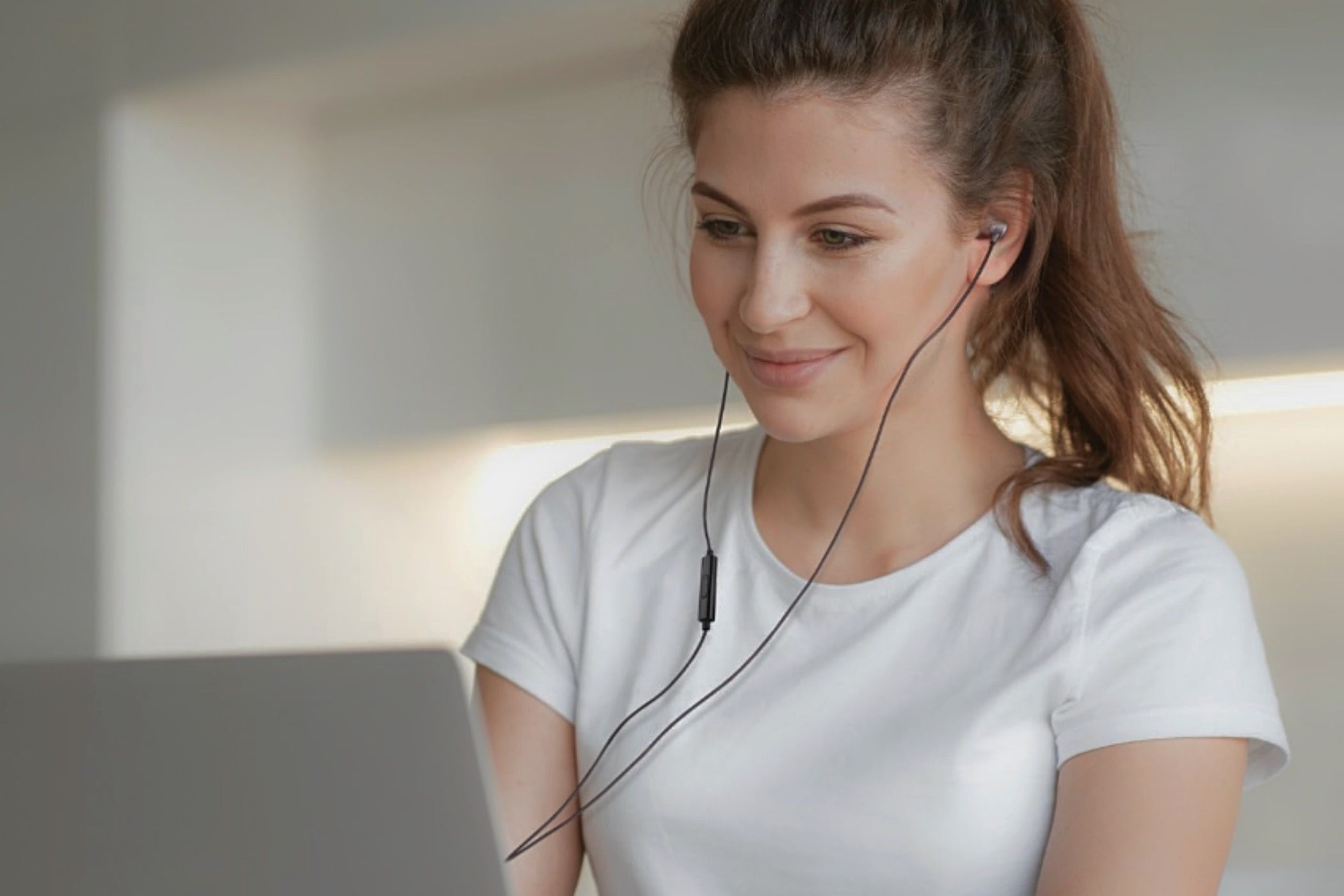 A woman on her laptop with a pair of UliX Rider earbuds in her ear.