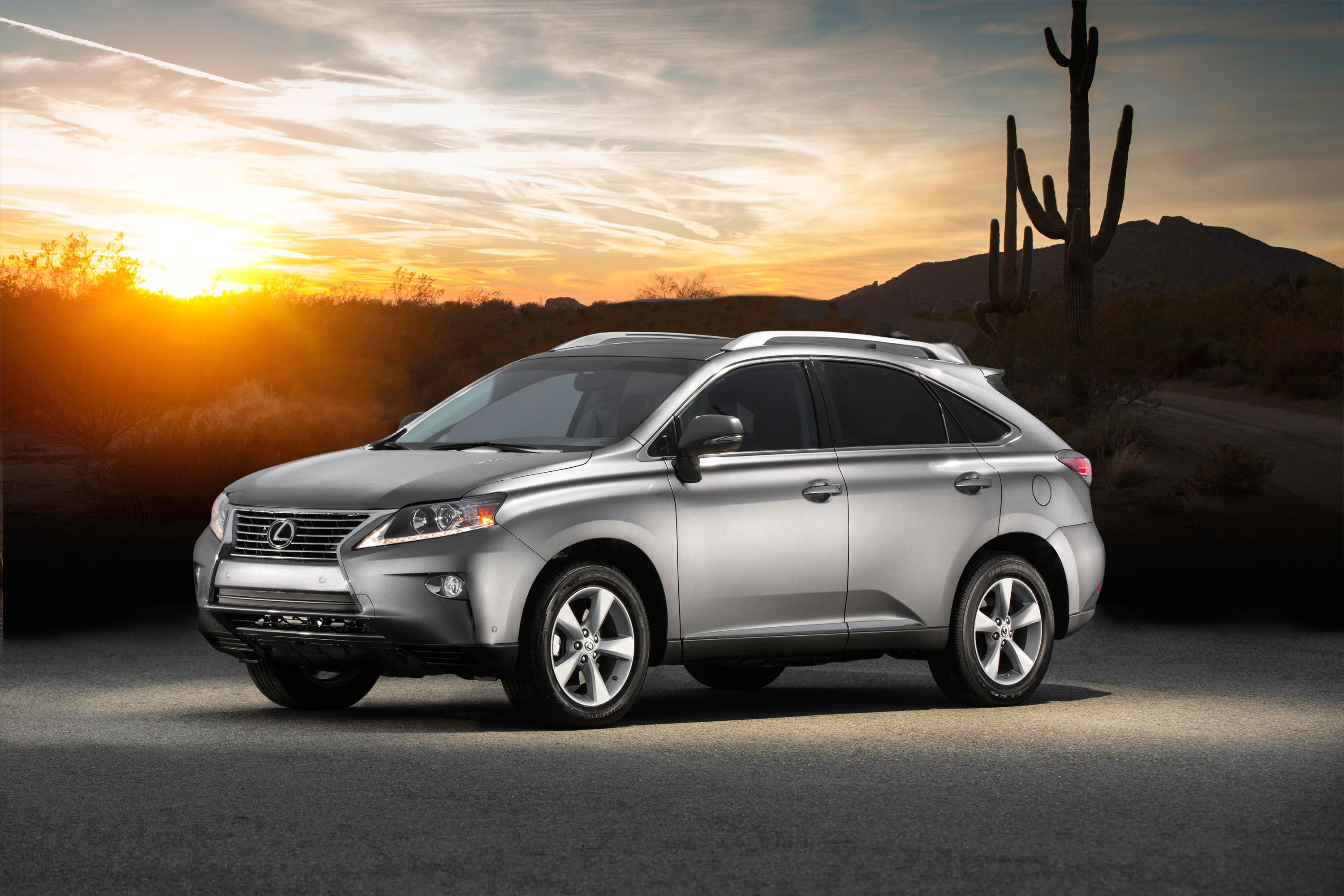 A silver 2014 Lexus RX 350 pictured parked with a desert scene behind it as the sun sets.