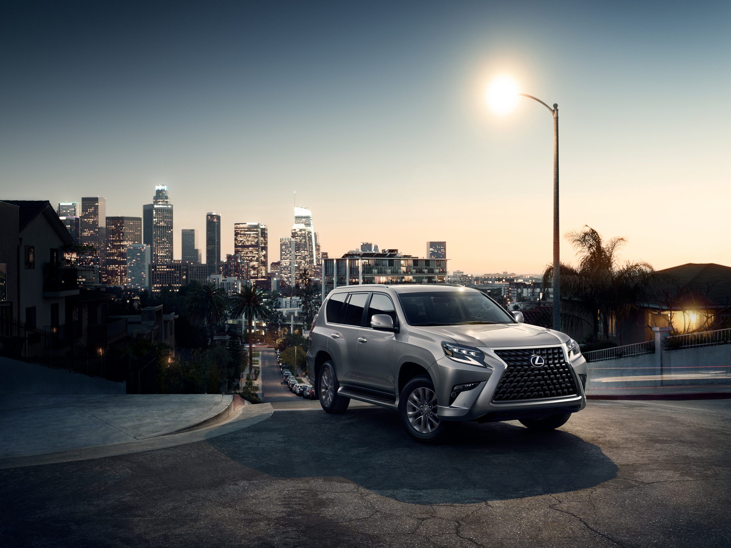 A silver 2022 Lexus GX 460 pictured parked on a street beneath a streetlight with the cityscape behind it.