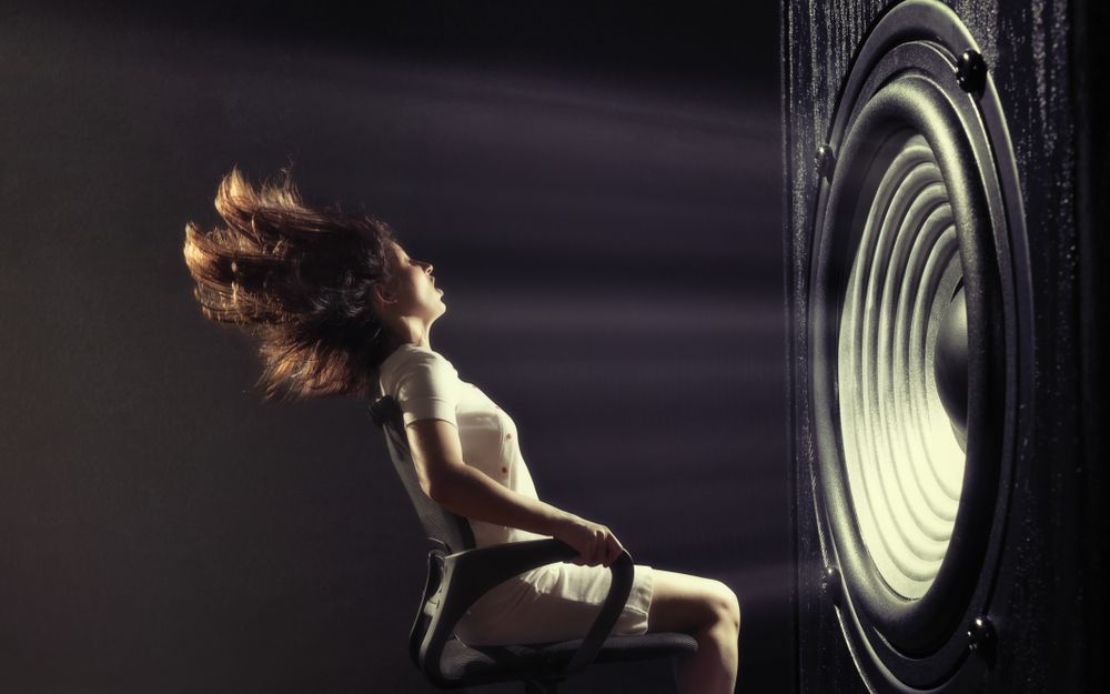 A woman being blown away by the sound from a giant speaker.