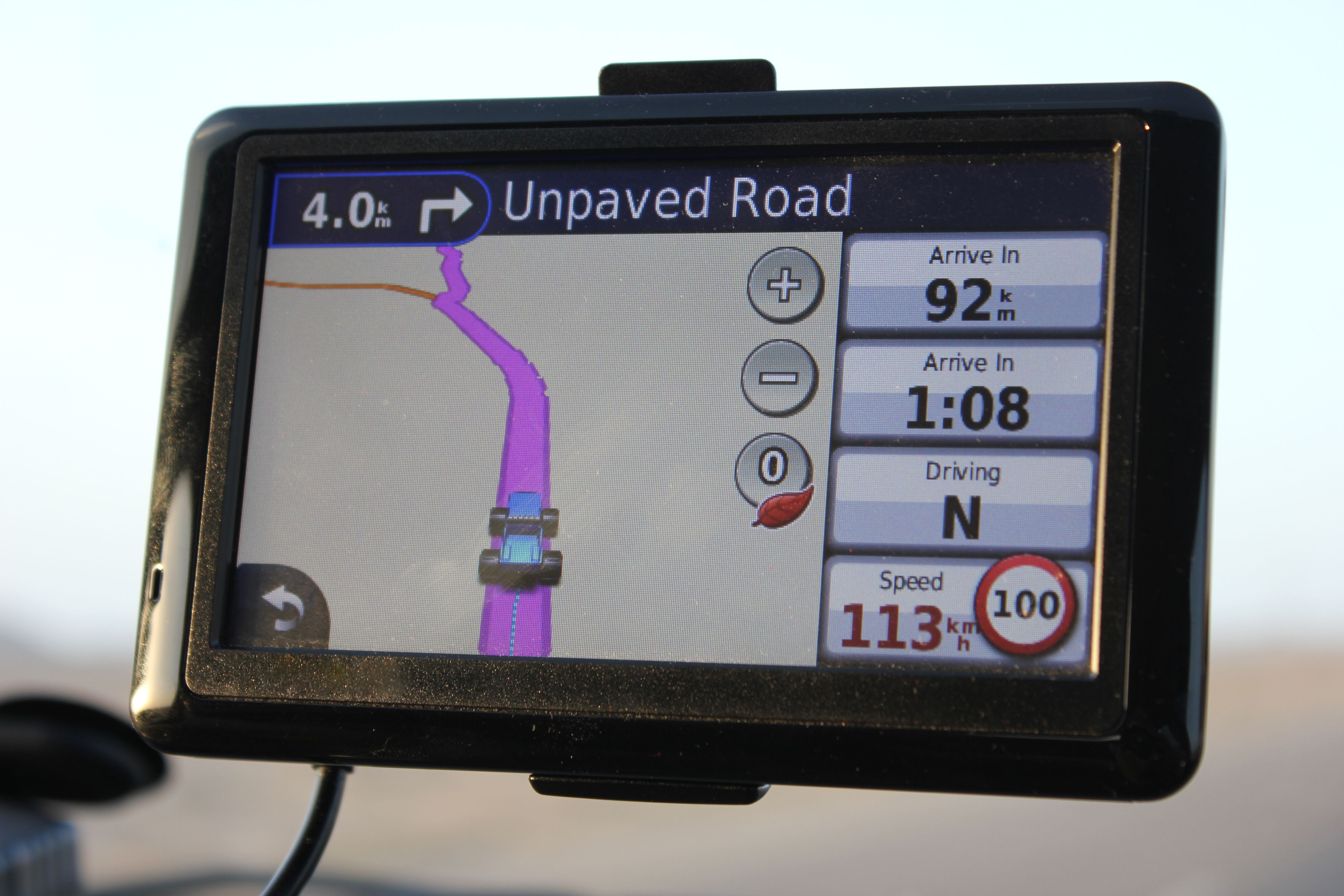A portable GPS device fixed to the windshield of a car, displaying vital driver information.