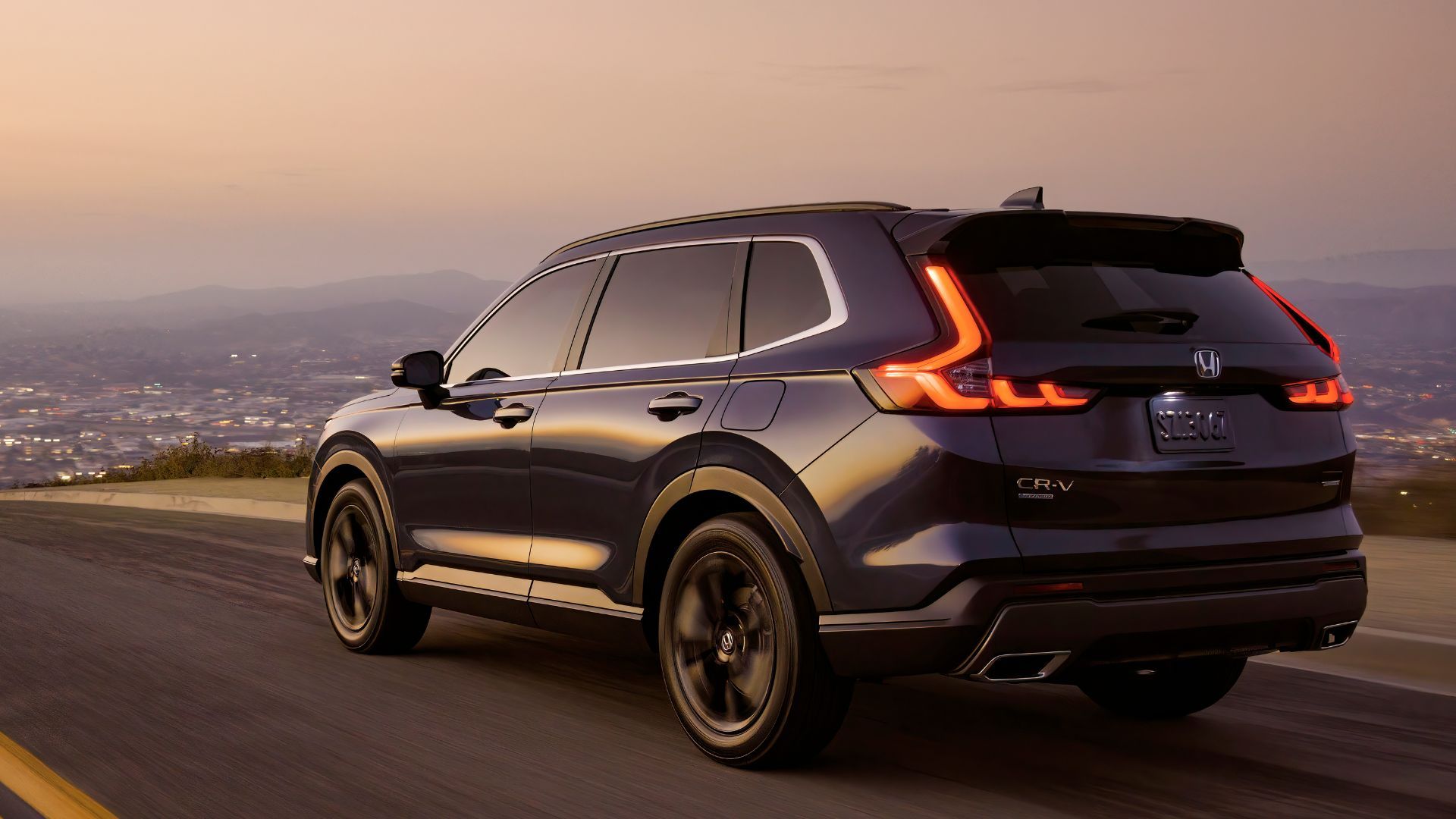 Dark blue Honda CR-V Sport Touring driving on a road with city lights in the background.