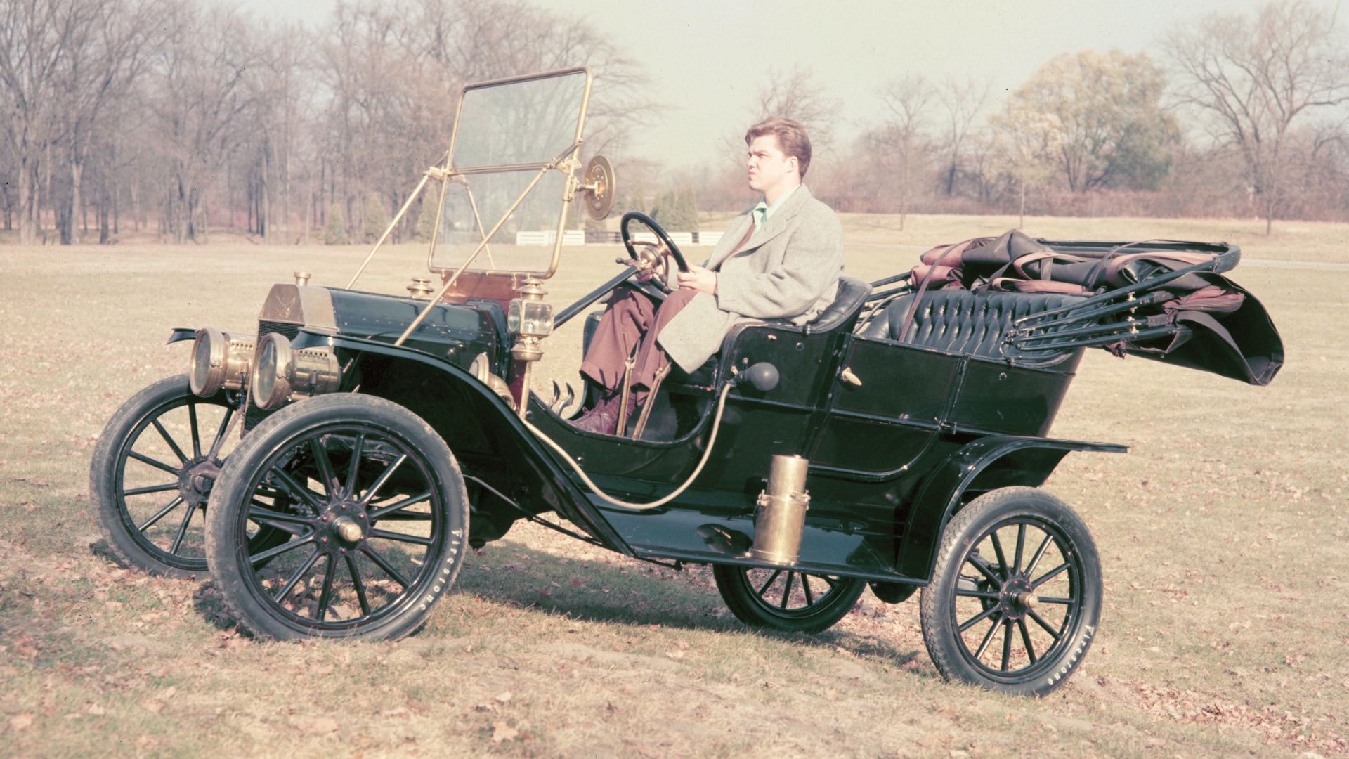 Side profile of a 1908 Ford Model T driving across grass in a field.