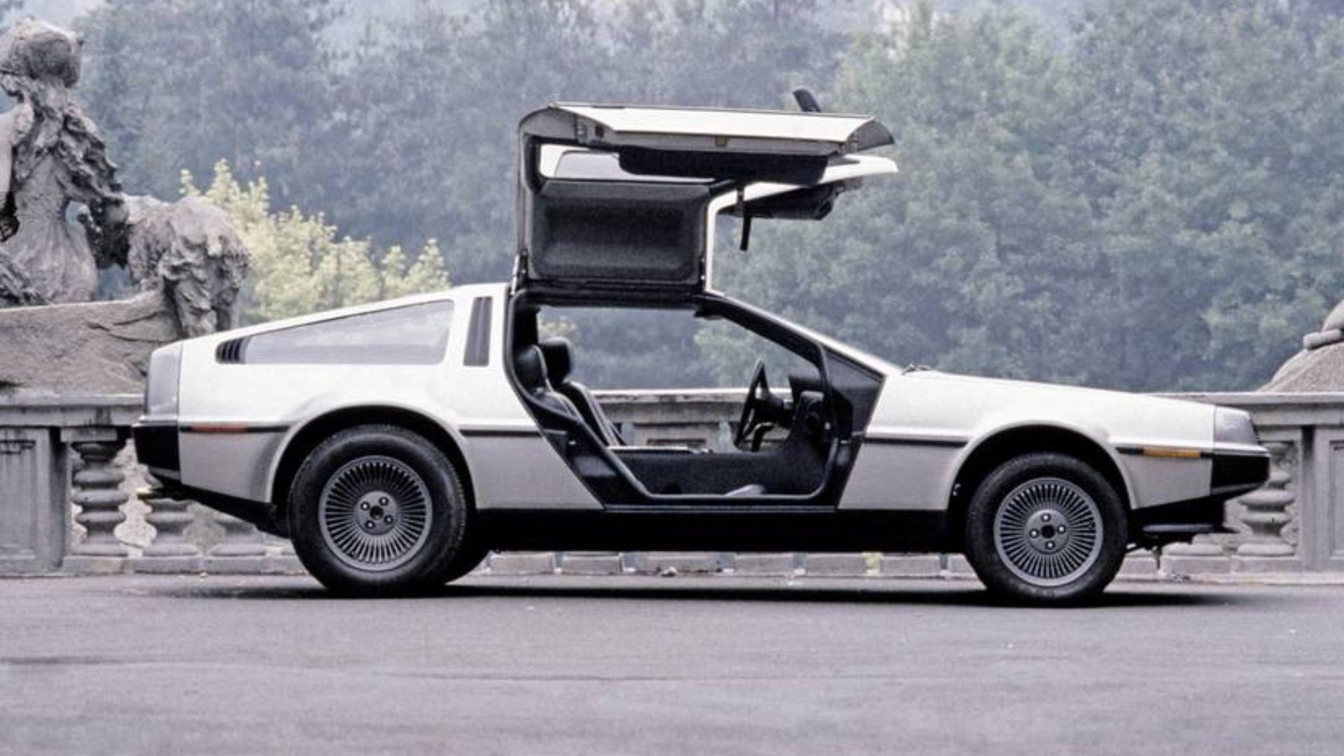 Side profile of a 1981 DeLorean DMC-12 with its gull-wing doors up.