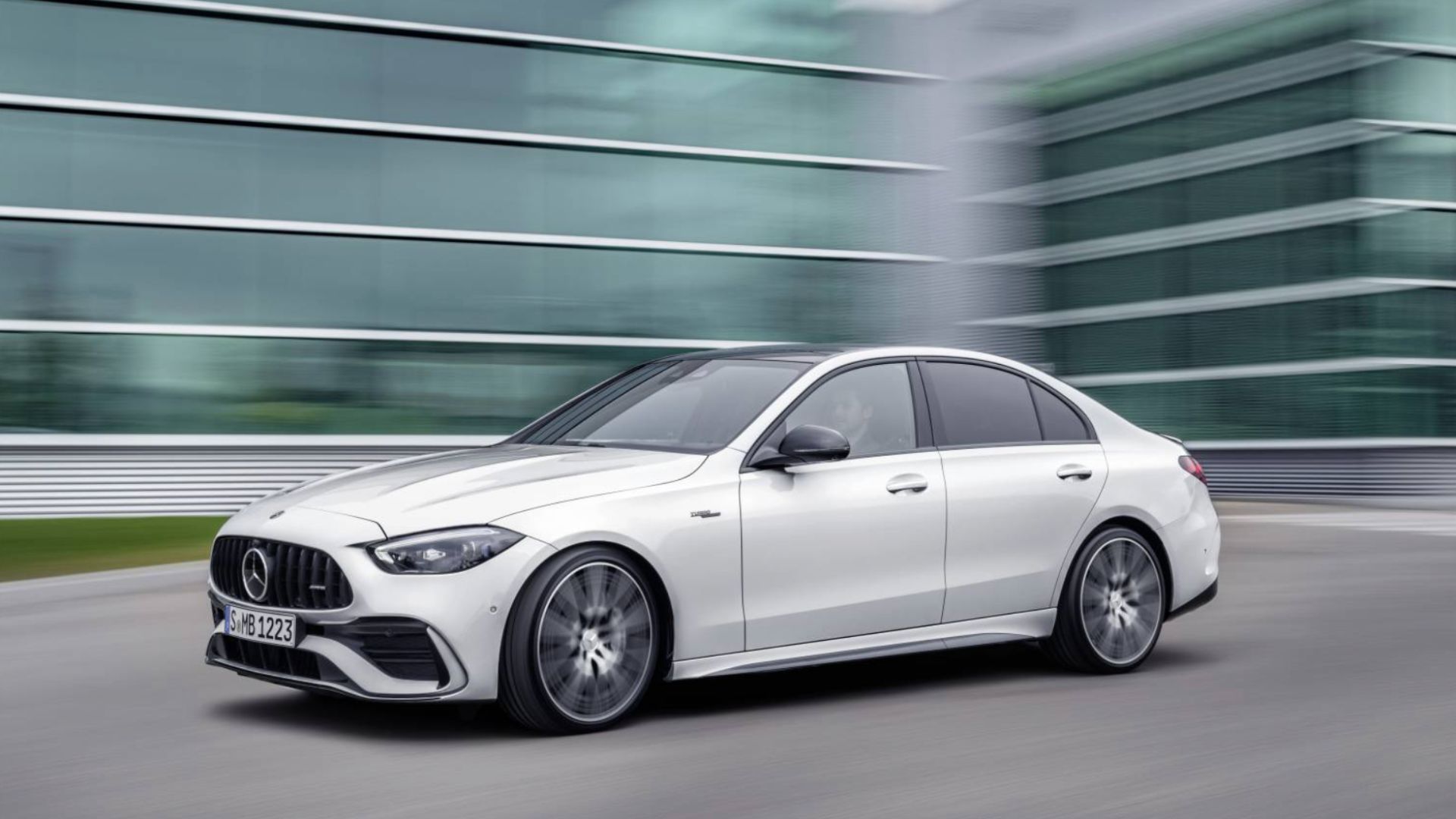 Full view of a white Mercedes-AMG C43 driving through a city with modern architecture in the background.