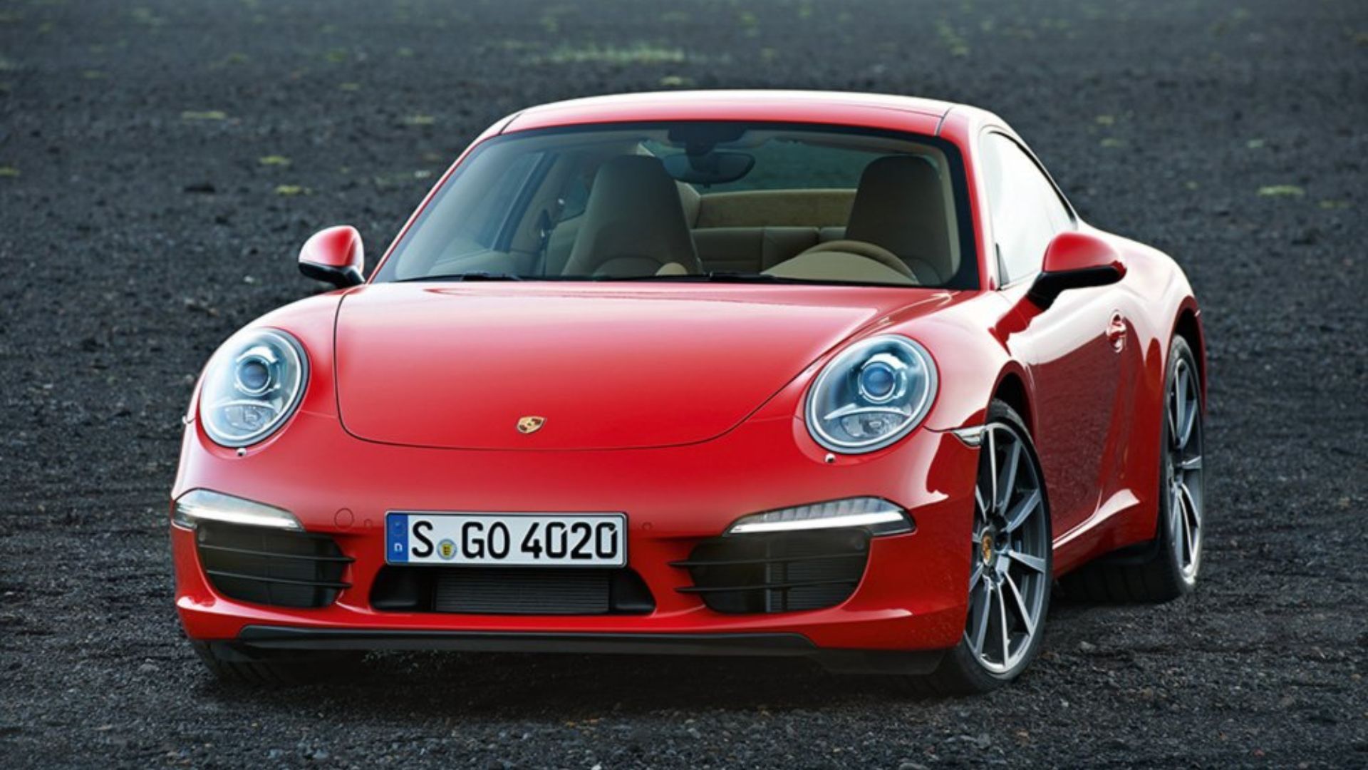 Red 2012 Porsche 911 Carrera 991 front end parked on gravel.