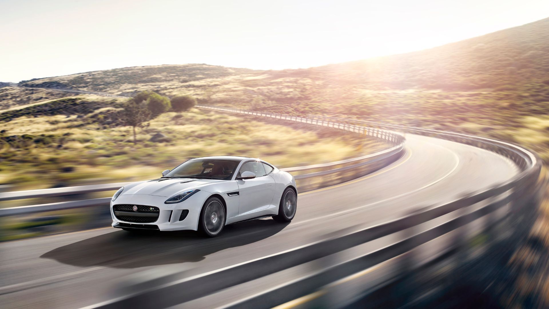 White 2014 Jaguar F-Type R Coupé driving on winding country road.