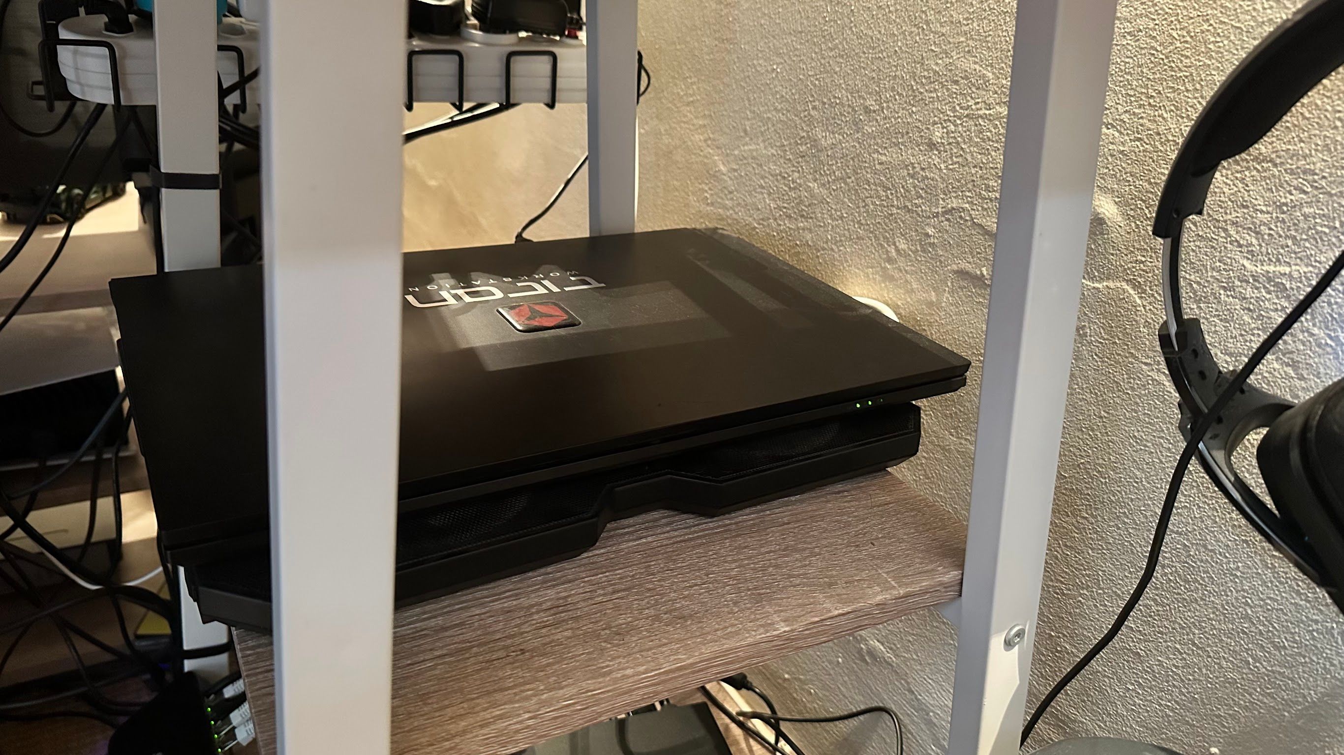 A closed laptop on a laptop cooler placed on a desk shelf.