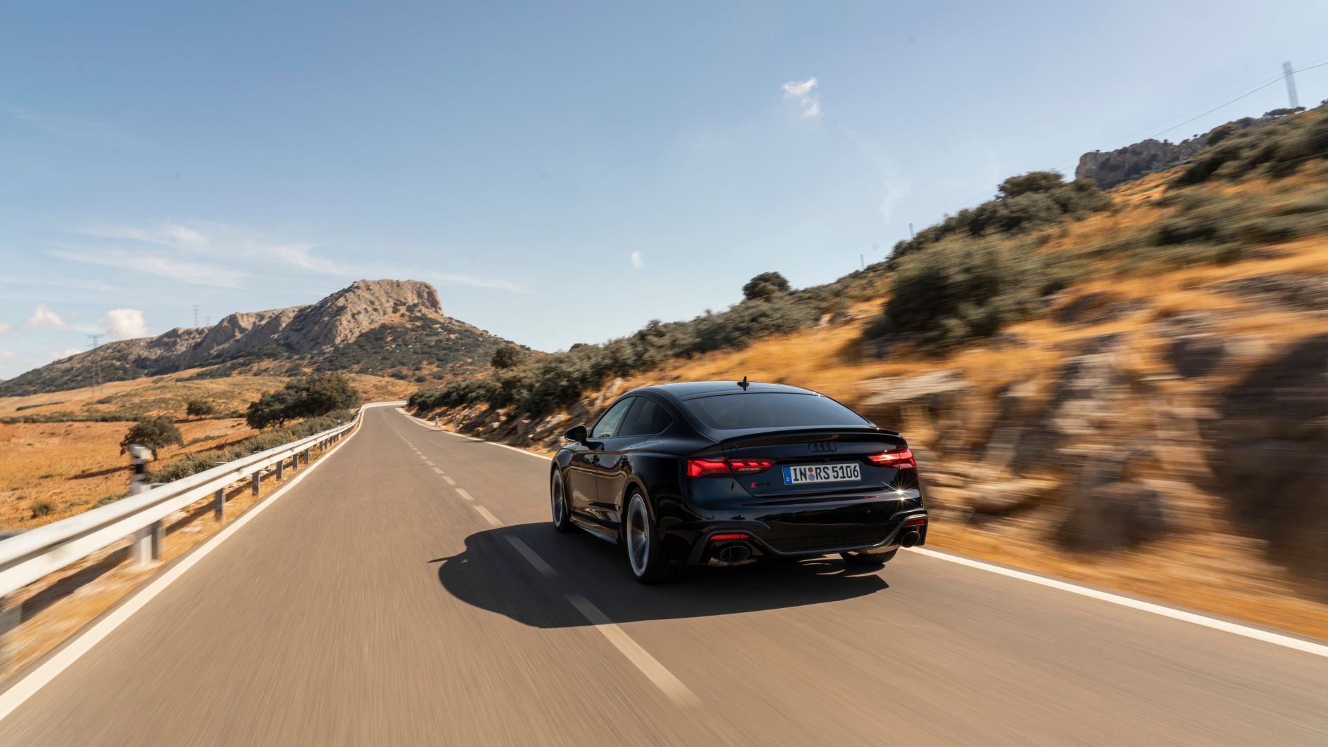 Rear view of Audi RS5 Sportback driving on a winding country road.