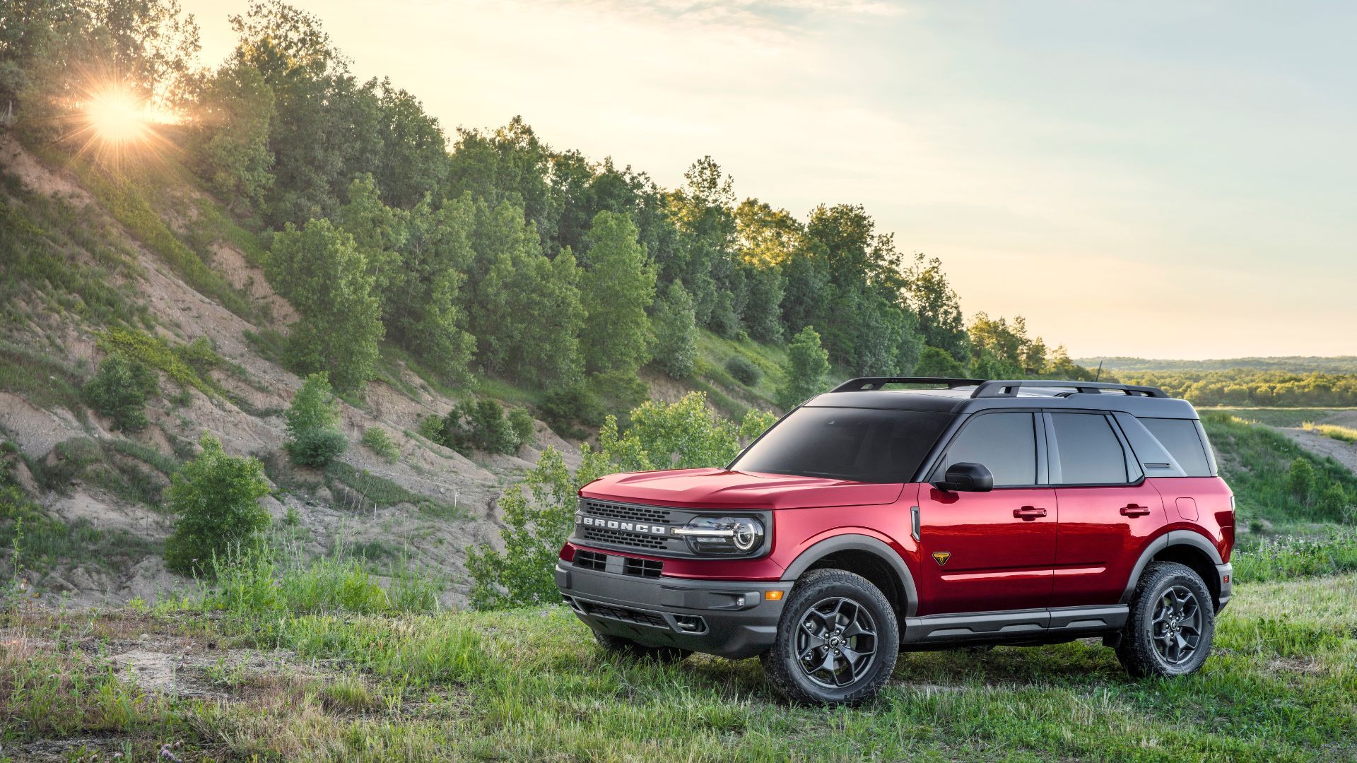 Full view of a red 2021 Ford Bronco Sport parked on grass with trees behind it.