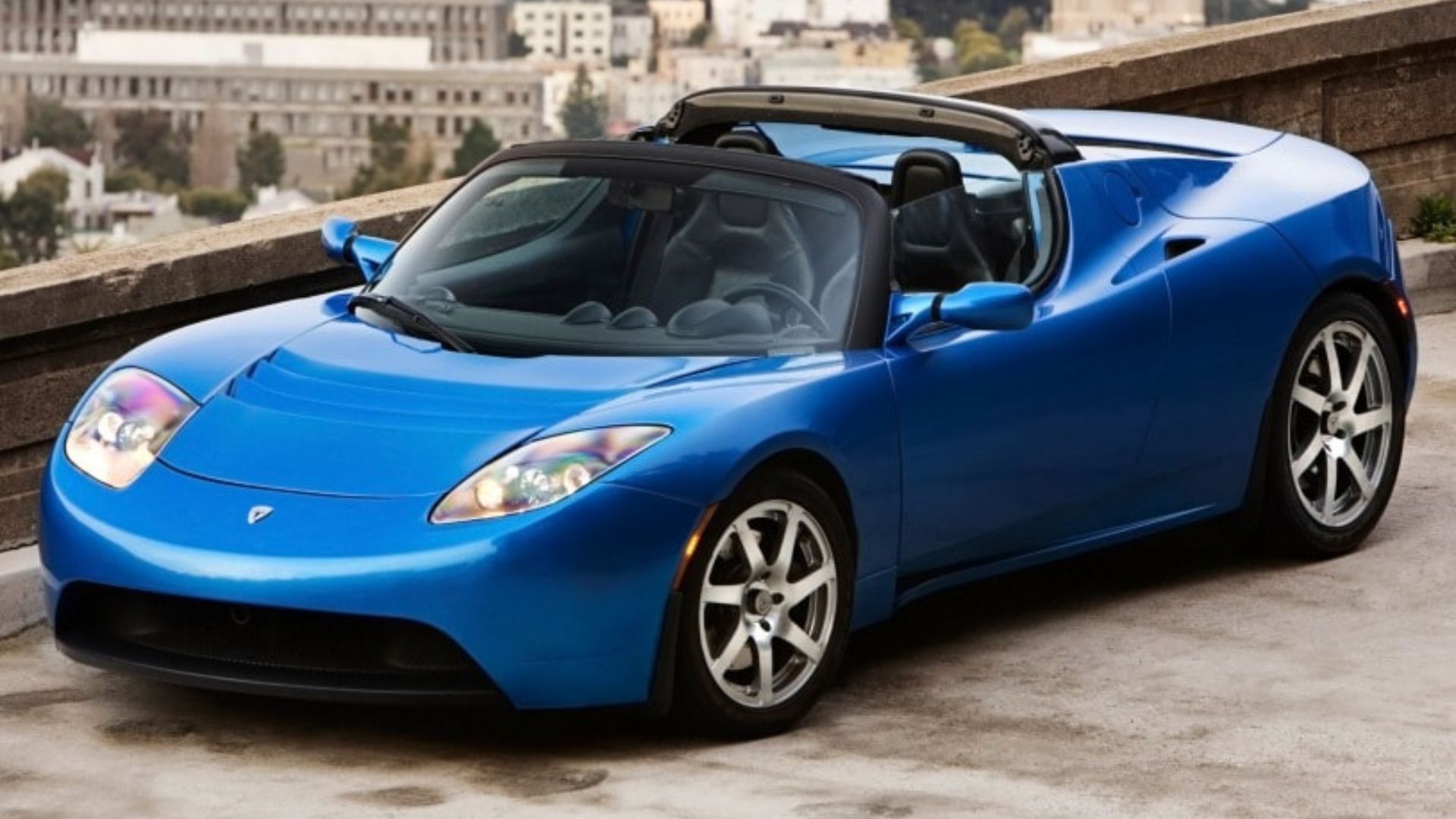 Full view of a blue first-generation Tesla Roadster parked on a rooptop.