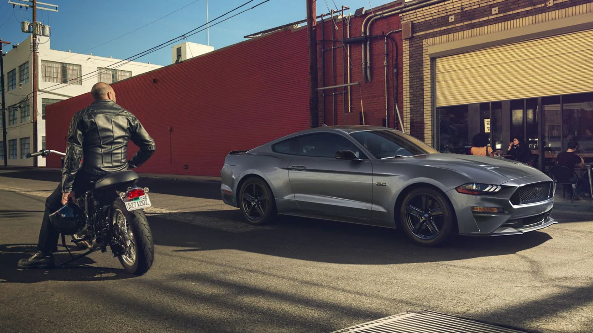 Full view of Ford Mustnag GT alongside a man on a motorcycle.