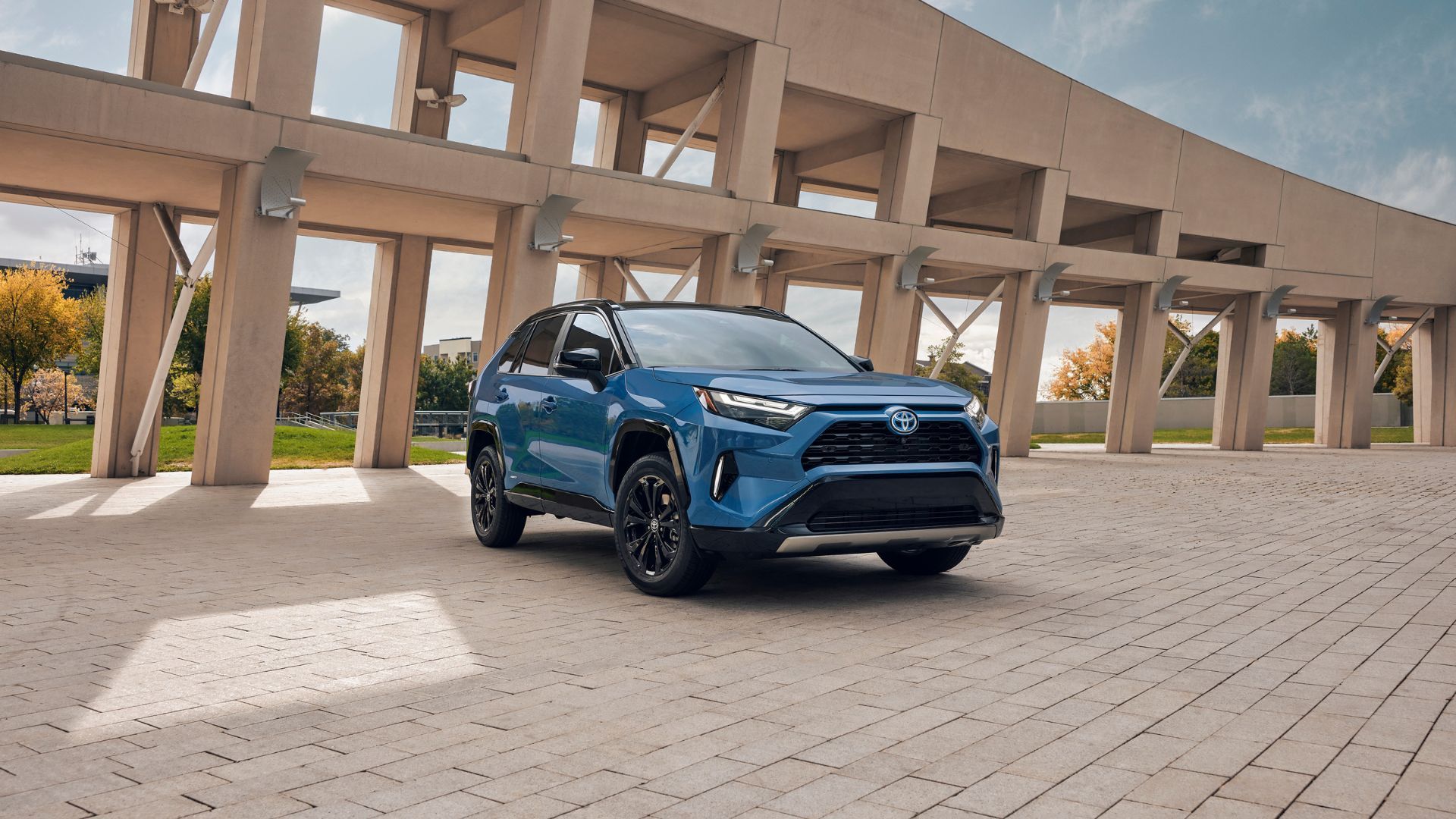 Blue 2024 Toyota RAV4 Hybrid parked on cobble stones with structure in the background.