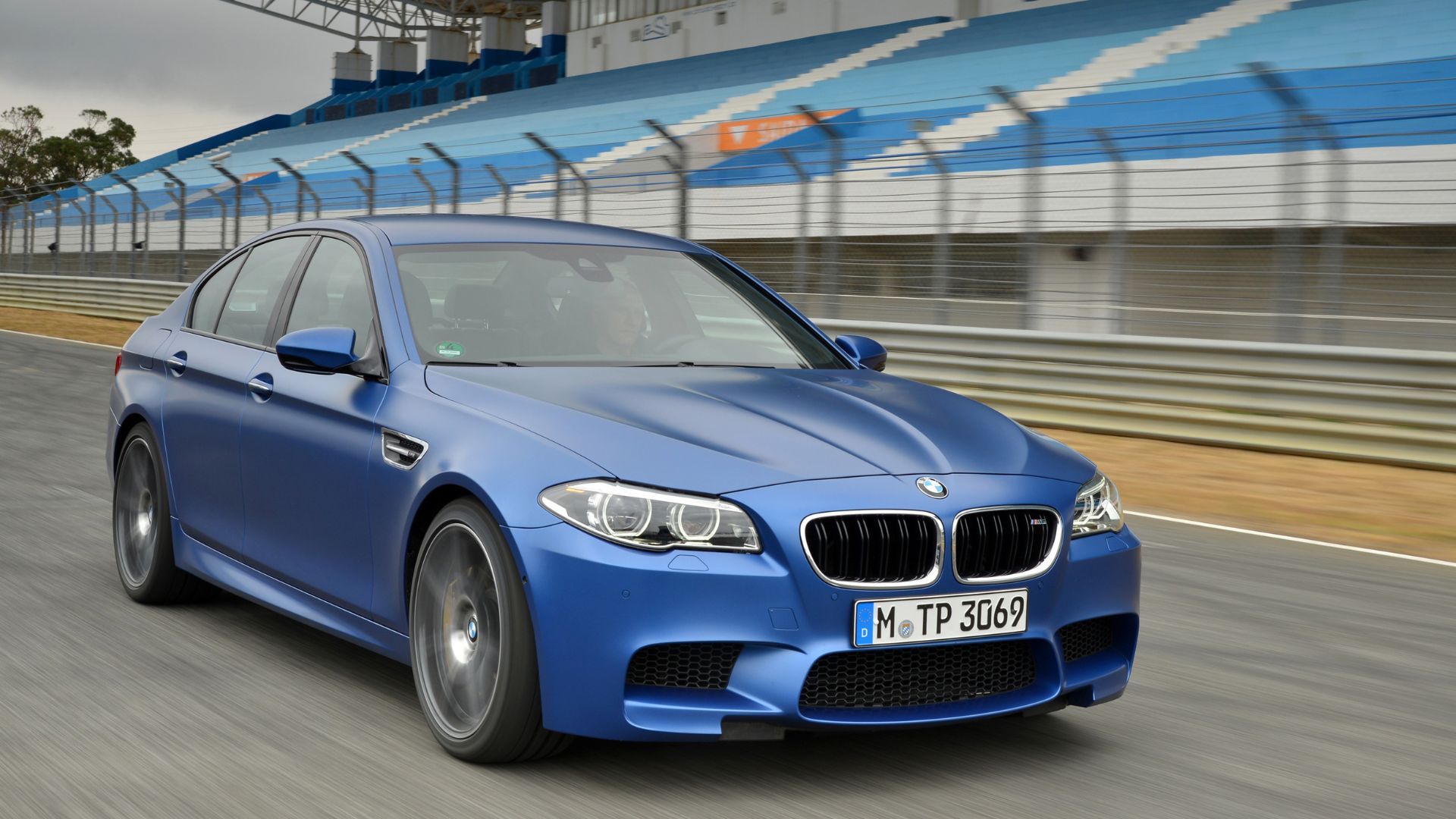 Full view of a blue 2013 BMW M5 driving on a race track.